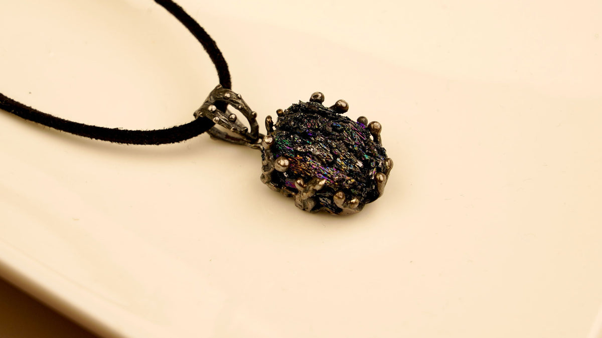 Raw black obsidian pendant in handcrafted sterling silver on a black cord, showing the natural iridescent surface of the stone
