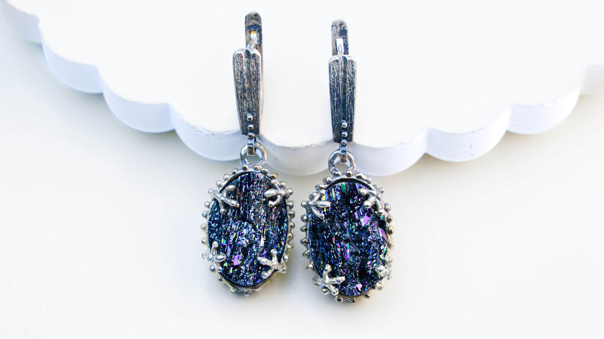 Two black tourmaline ovals hanging before a white scalloped edge, blue and violet catching in the broken surfaces