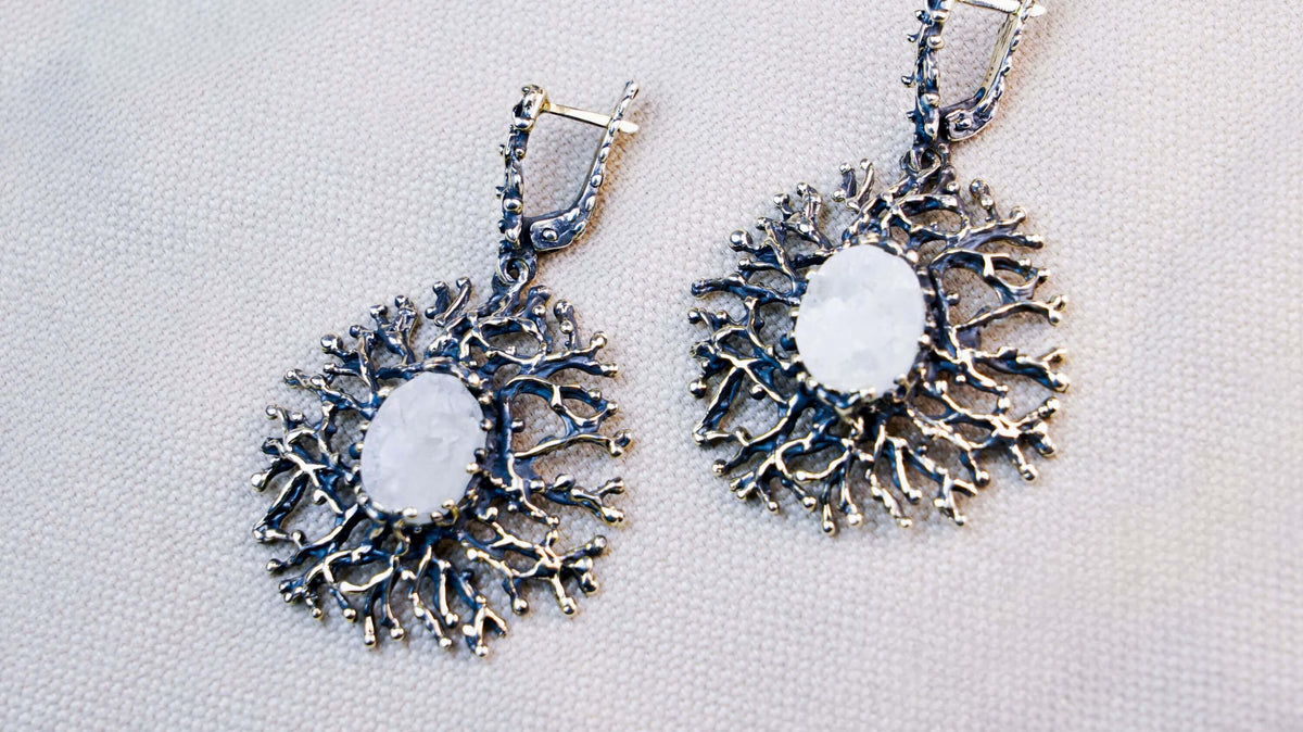 Two white moonstone ovals on textured cloth, each set in a round silver frame of fine branching arms