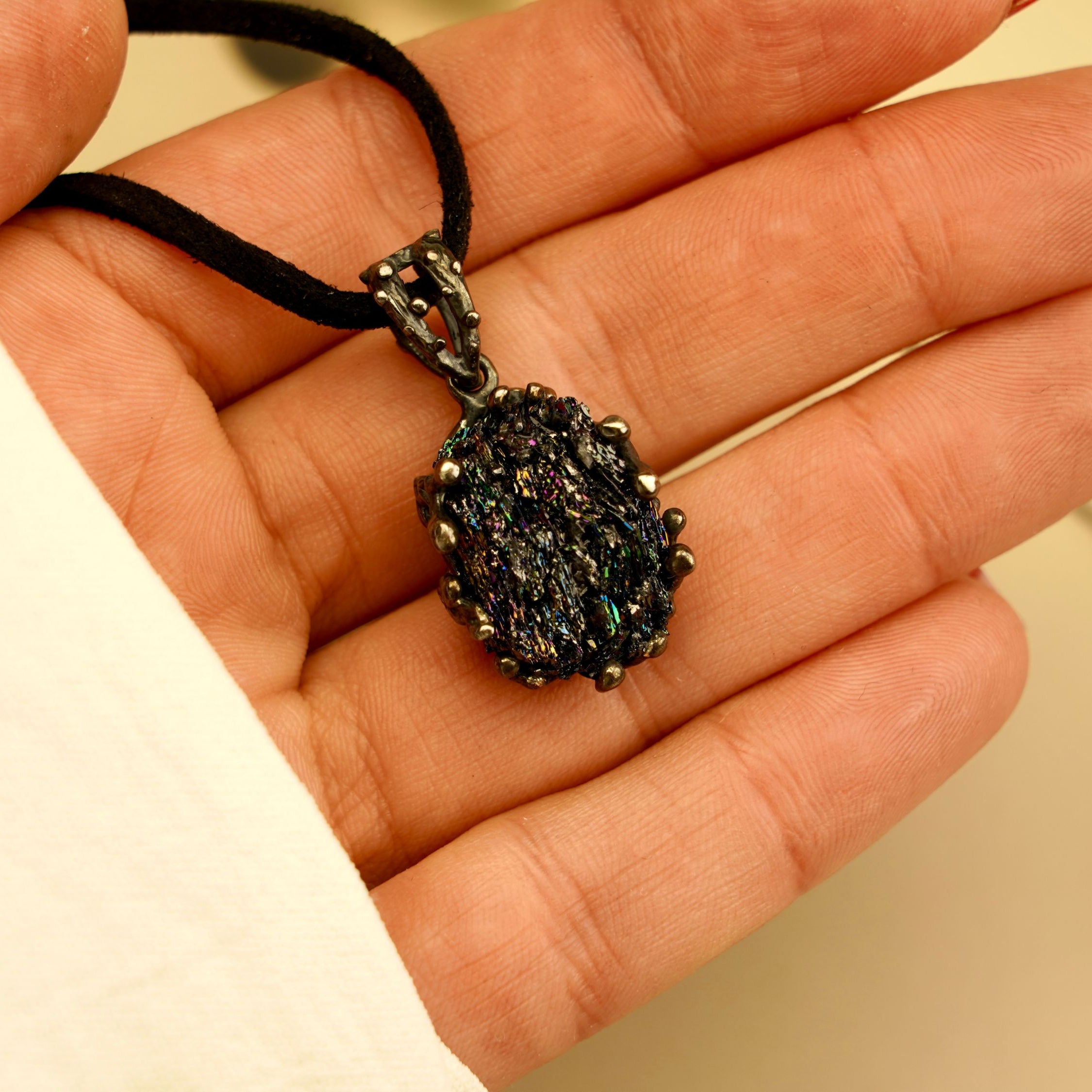 Close-up of a handcrafted raw black crystal pendant held in hand, showing the scale and unique texture of the Obsidian stone