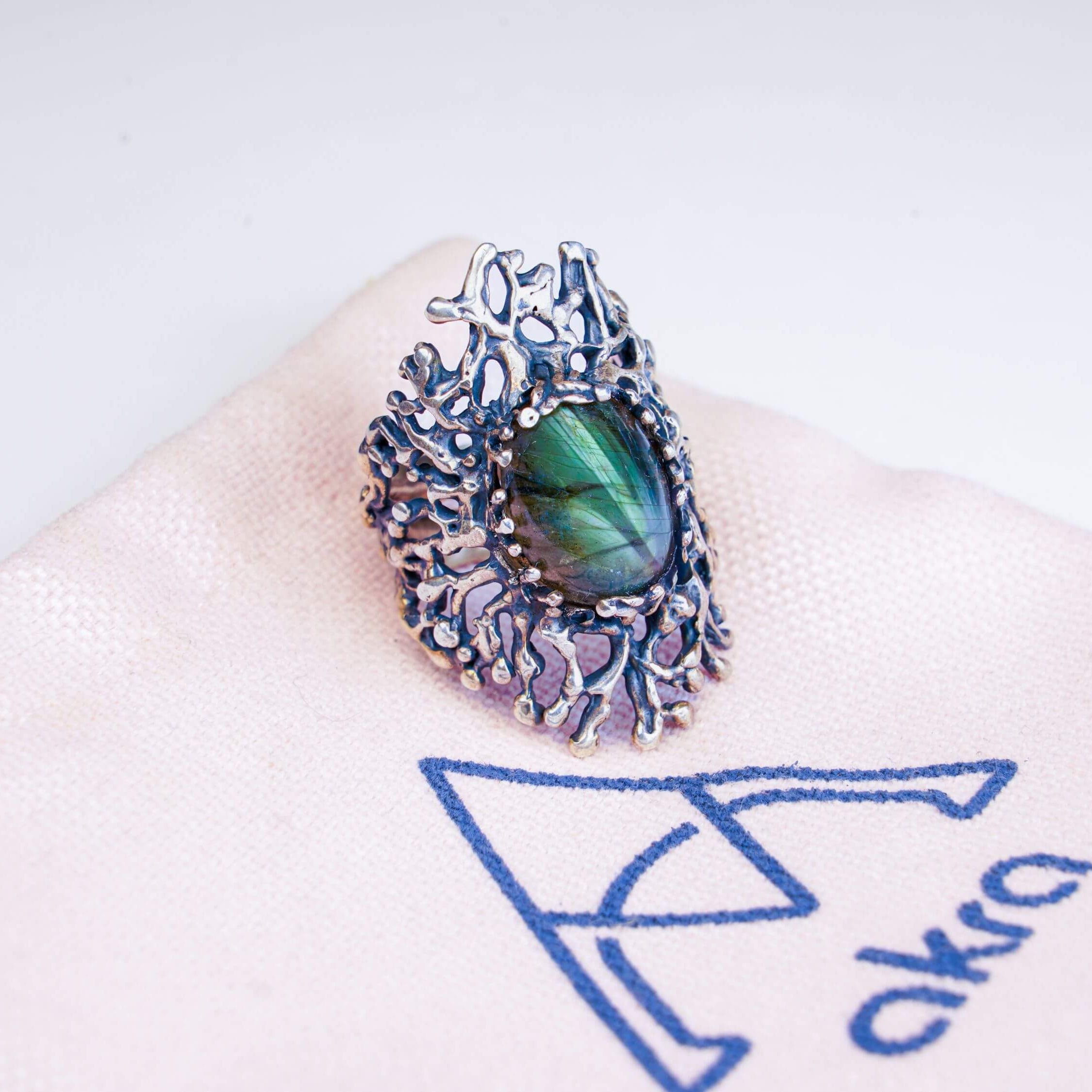 Mystical labradorite gemstone ring displayed on a branded Akra pink jewelry pouch