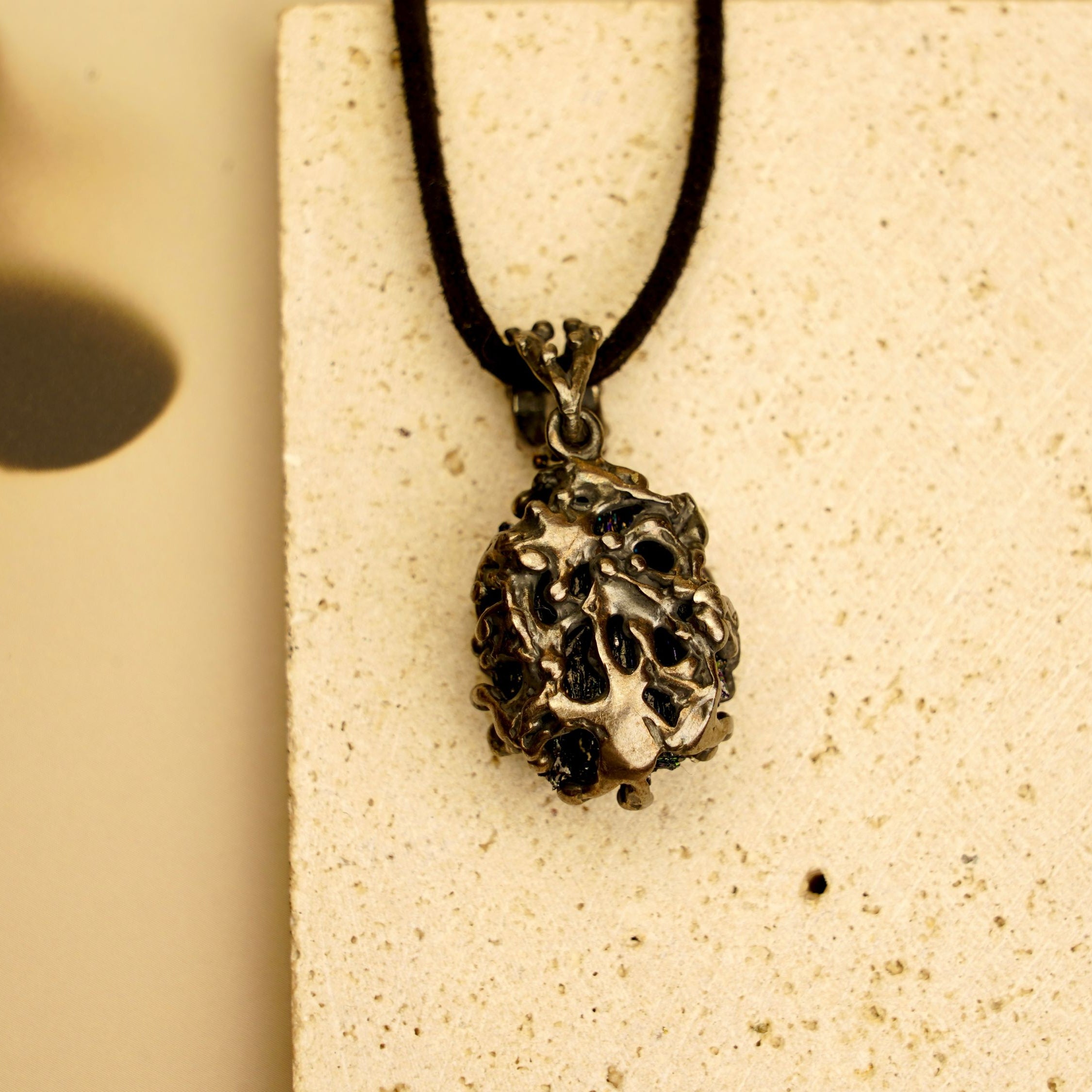 Perspective shot of the raw black crystal necklace, showing the metallic shimmer and unique silver cage design