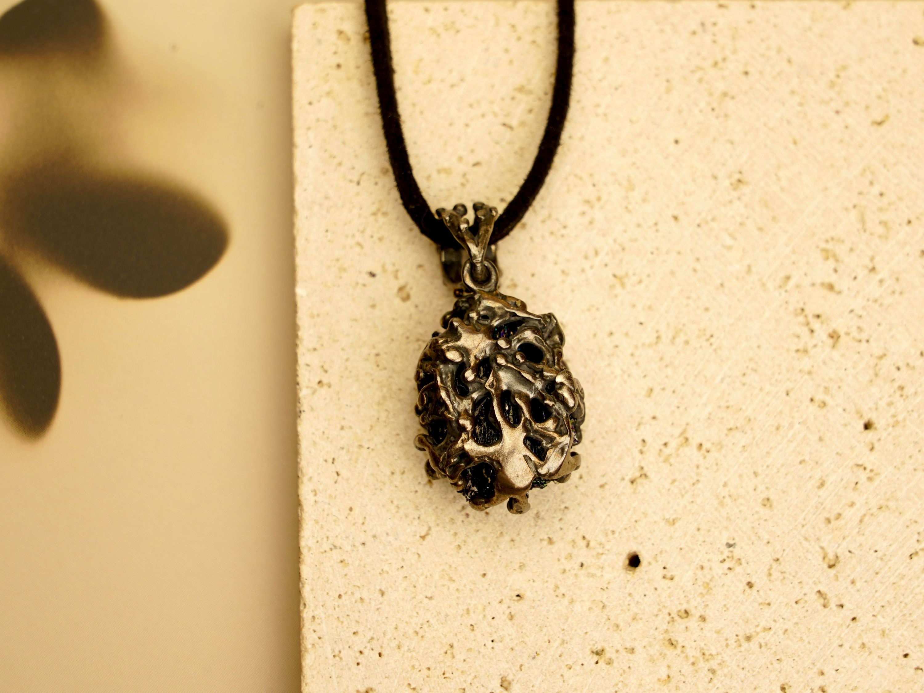 Perspective shot of the raw black crystal necklace, showing the metallic shimmer and unique silver cage design