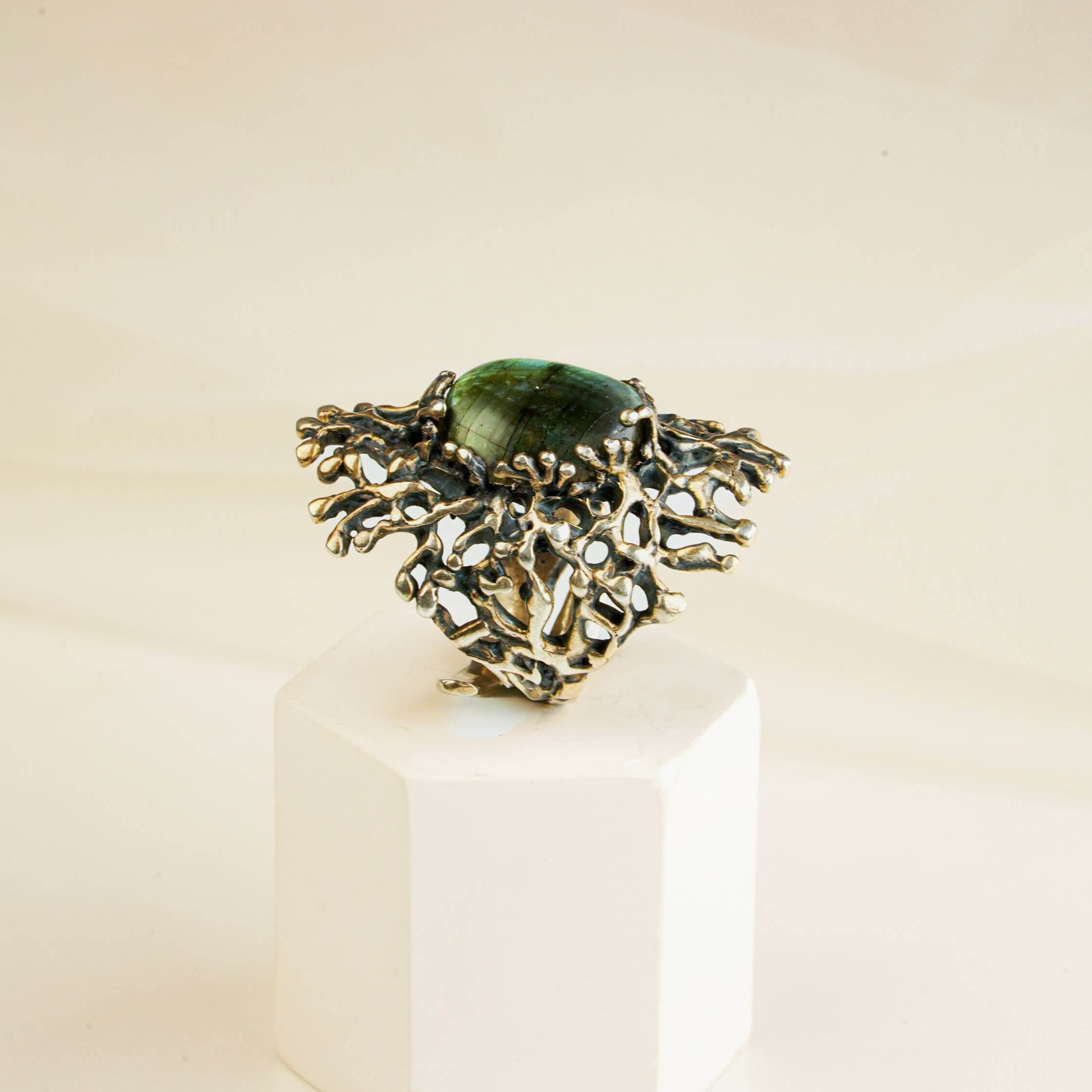 Artistic presentation of a rectangular iridescent labradorite ring on a white aesthetic pedestal