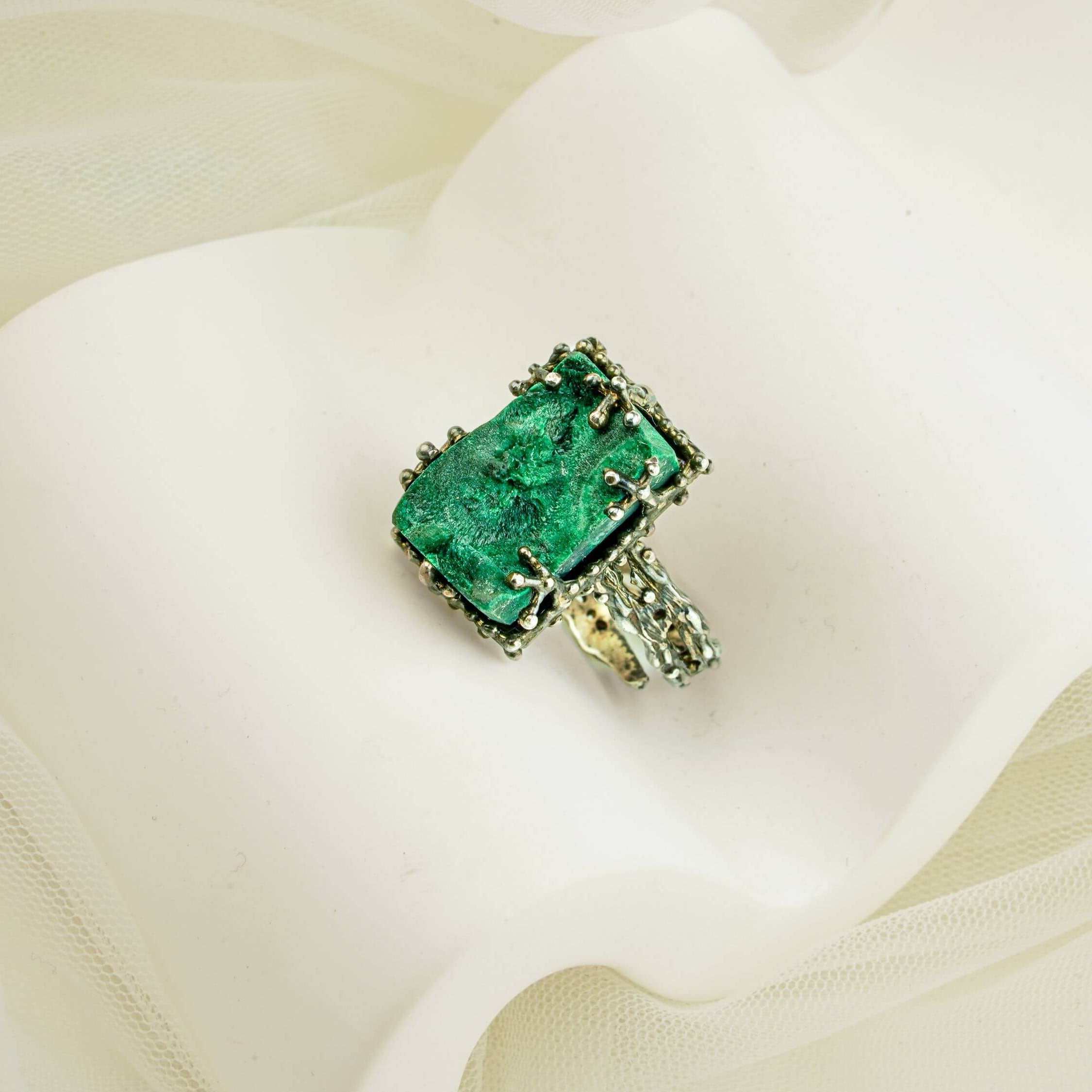 Artistic shot of a bold green malachite statement ring nestled in soft white fabric folds
