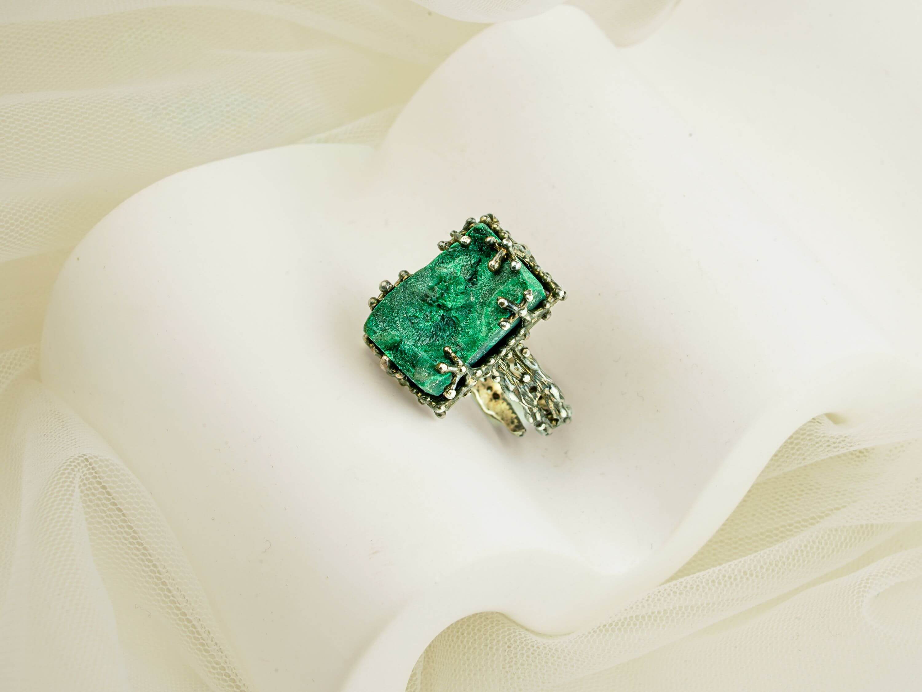 Artistic shot of a bold green malachite statement ring nestled in soft white fabric folds