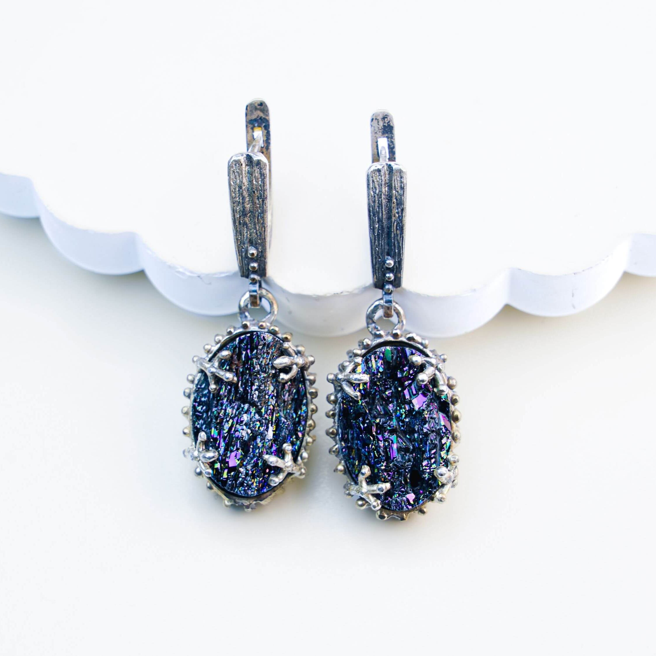 Oval Black Tourmaline earrings featuring raw crystalline gemstones in an ornate sterling silver frame, shot on a clean beige background