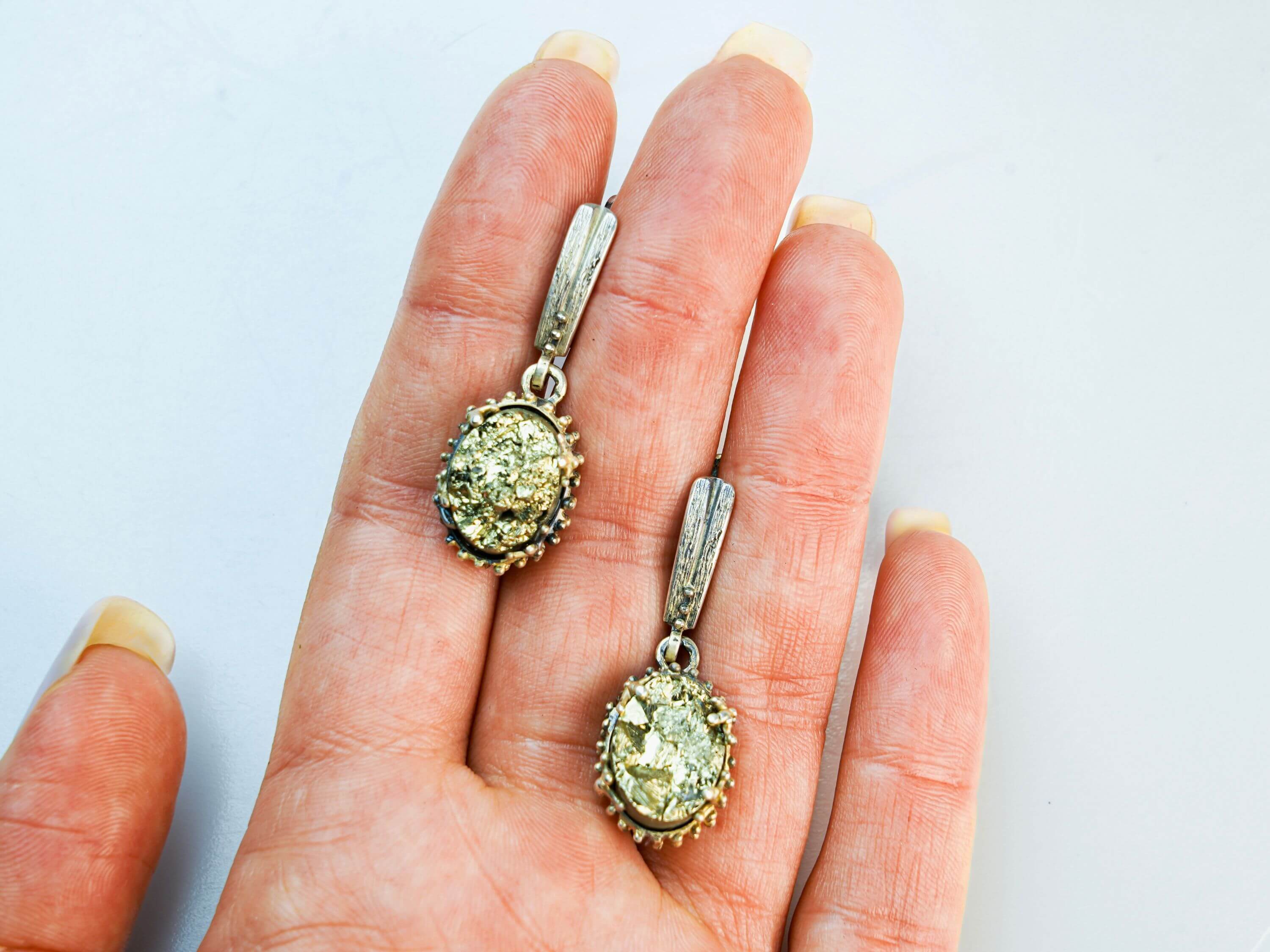 Two golden pyrite statement earrings held in a hand to illustrate their perfect oval scale and handcrafted silver detailing