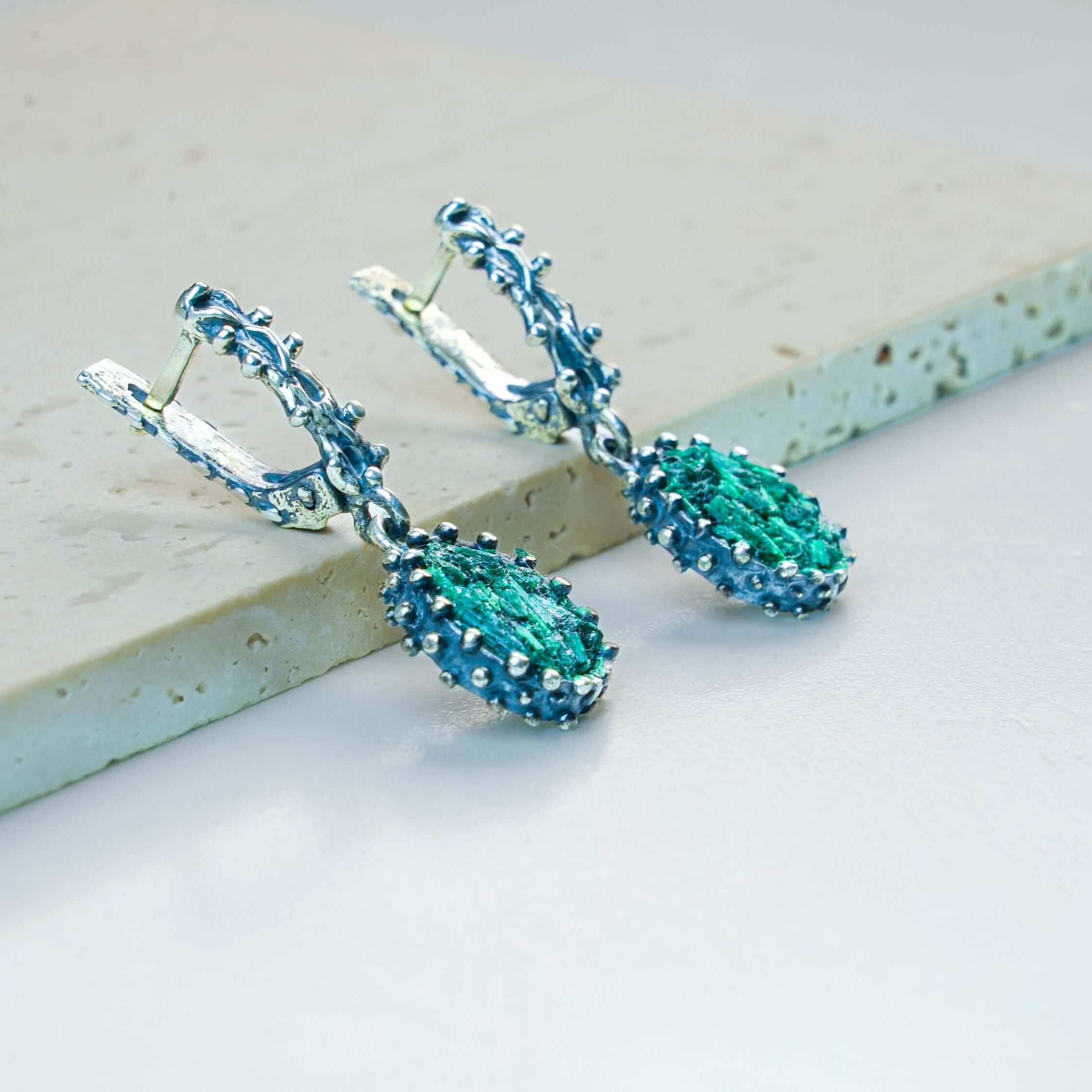 Handmade Akra Gems Malachite earrings resting alongside other pieces from the green gemstone collection, crafted in Tbilisi, Georgia