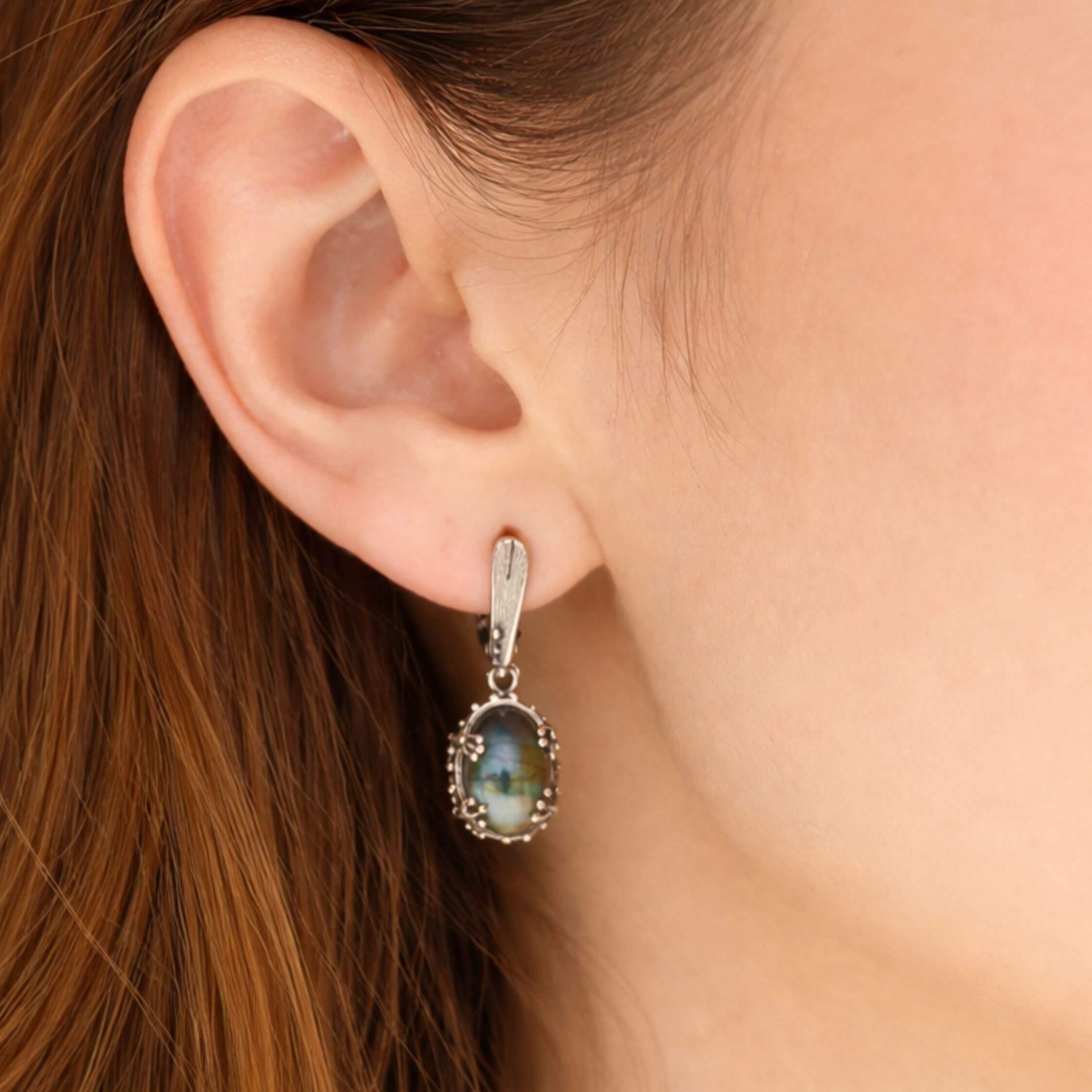 Handmade labradorite earrings worn on ear, showcasing the elegant drop style and blue gemstone flash
