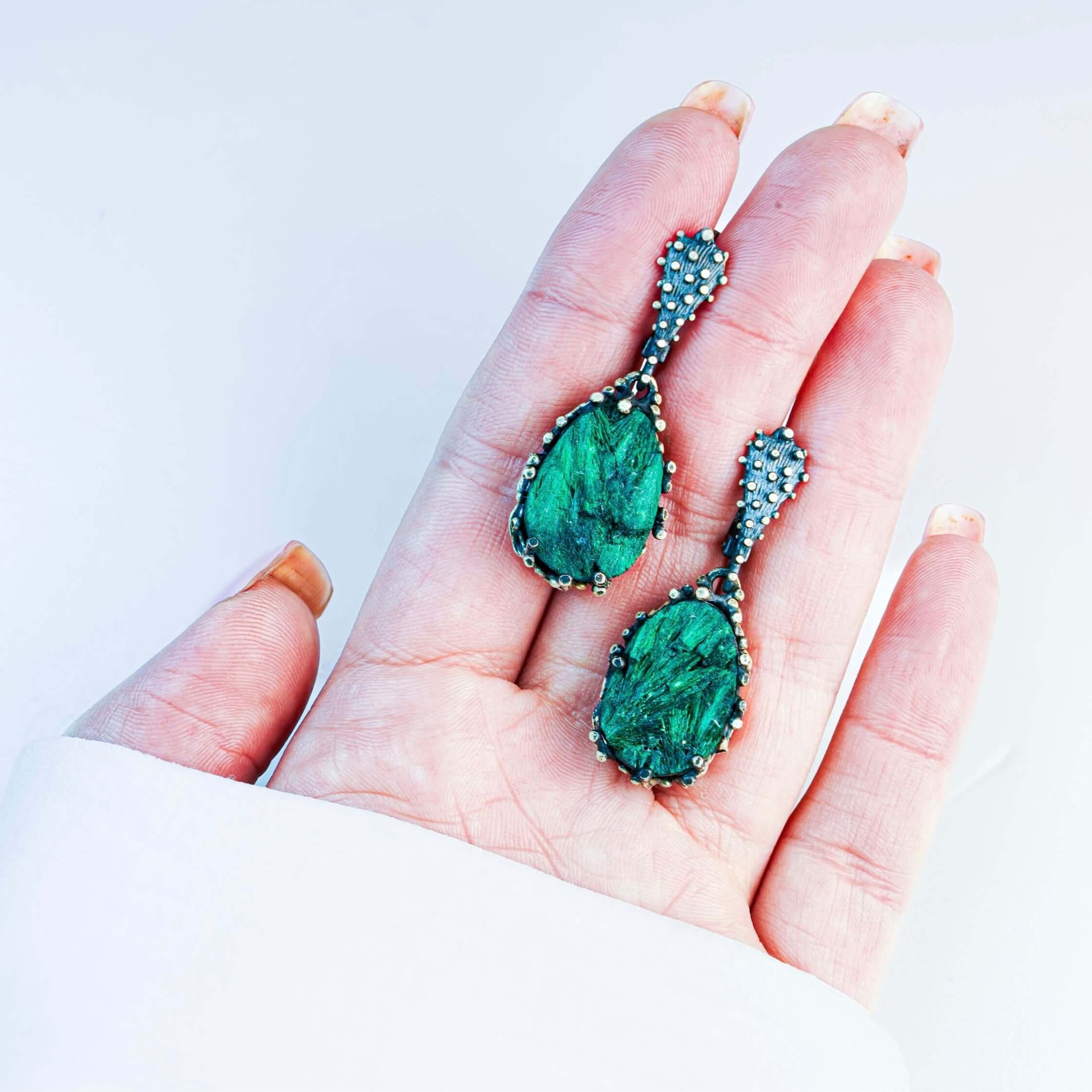 Handheld shot of both malachite dangles, demonstrating the bold statement size and handcrafted silver frame