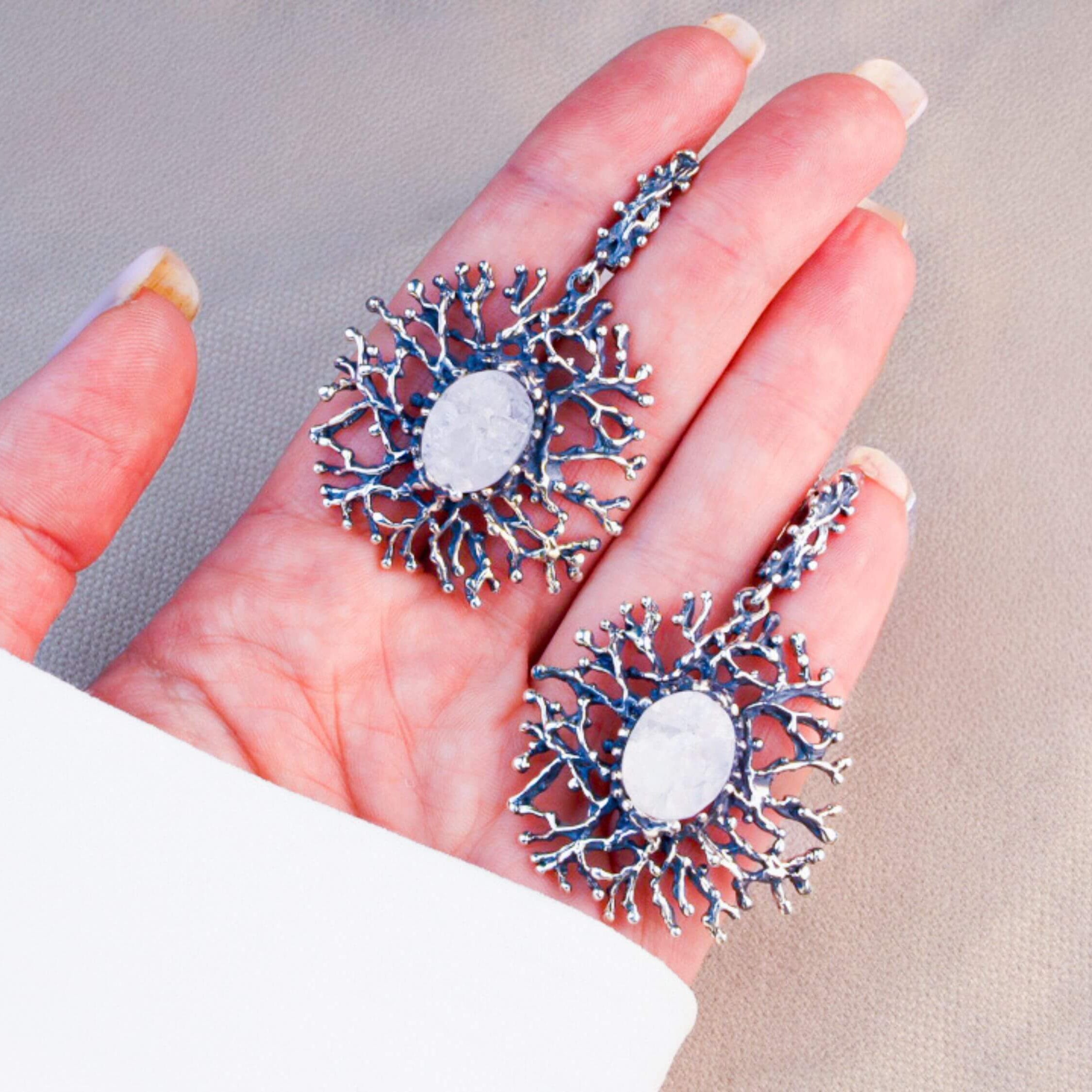 A pair of large Moonstone branch earrings held in a hand to demonstrate their impressive statement size and artisan quality