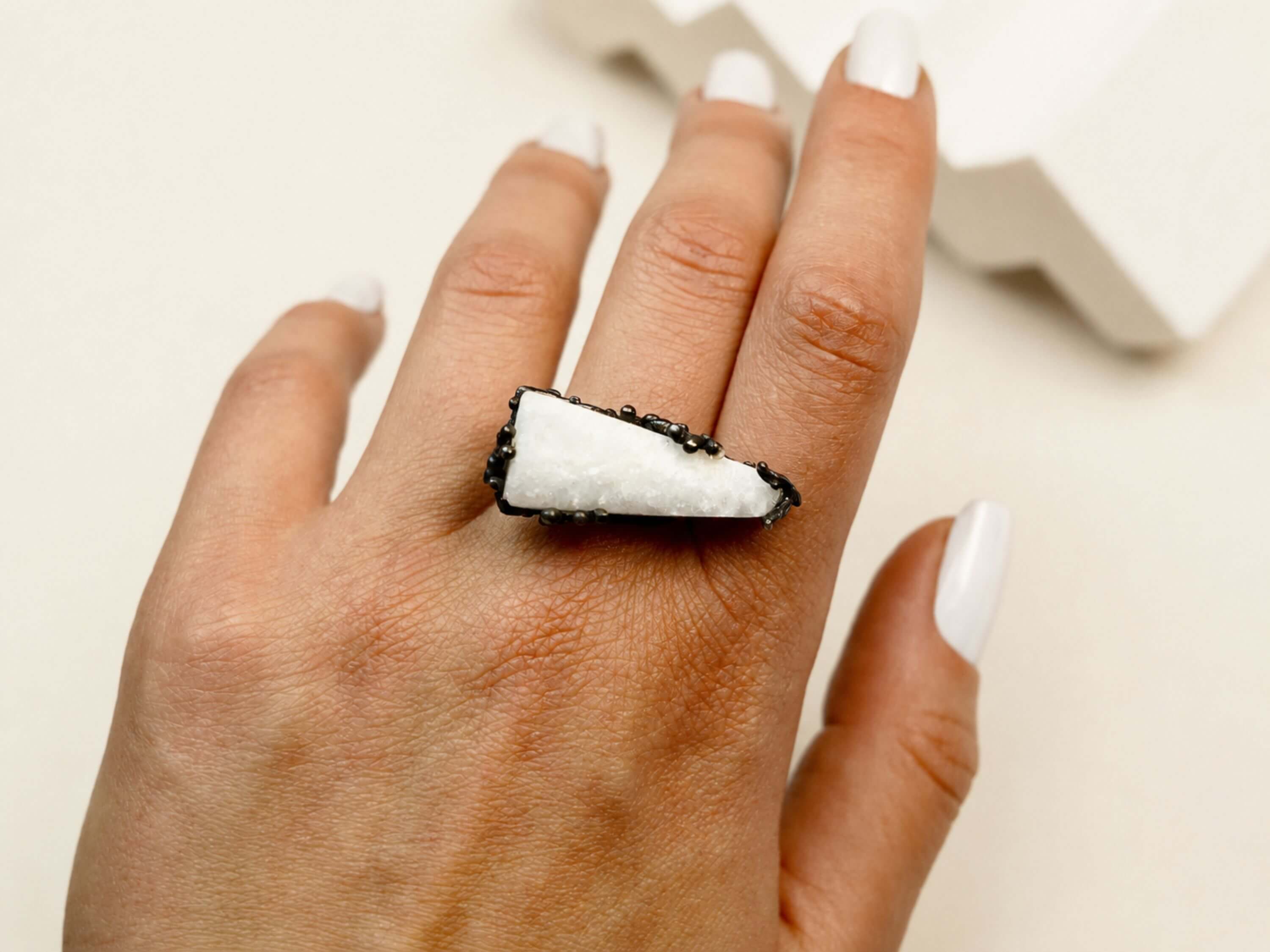 A model wearing the large raw Moonstone ring, showcasing the striking contrast between the white stone and the hand-textured dark silver band.