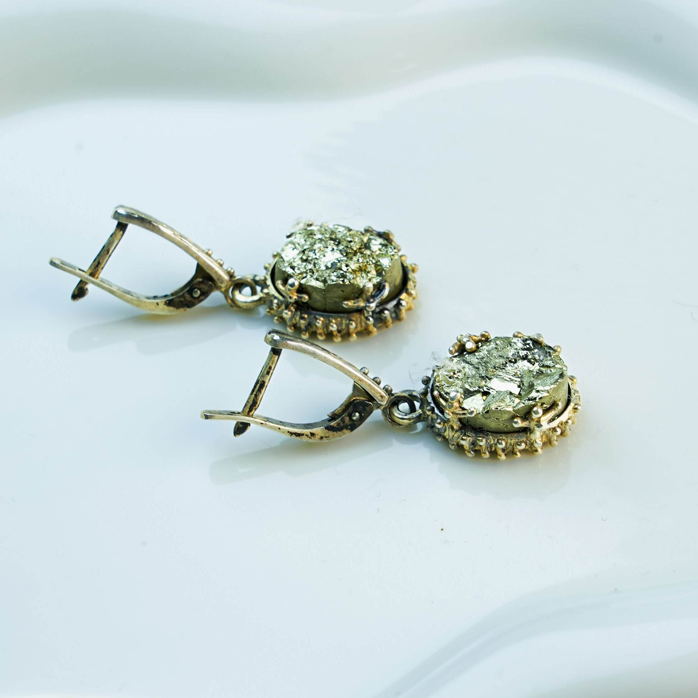 Side profile of the oval pyrite earrings, showing the depth of the stone and the intricate texture of the silver setting