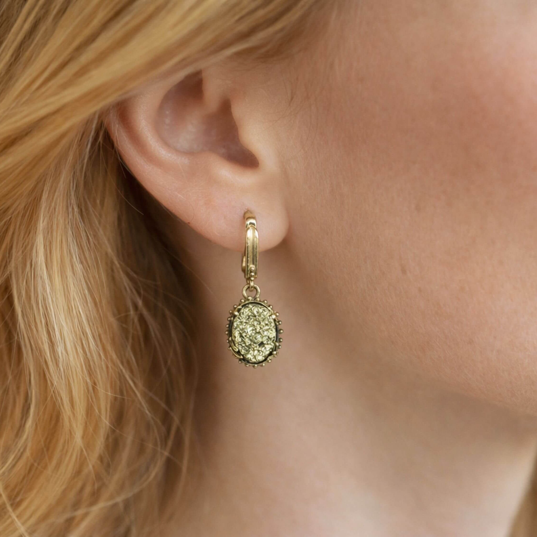 A model wearing Akra Gems golden pyrite earrings, showing the elegant oval drop and how the metallic shimmer complements the face