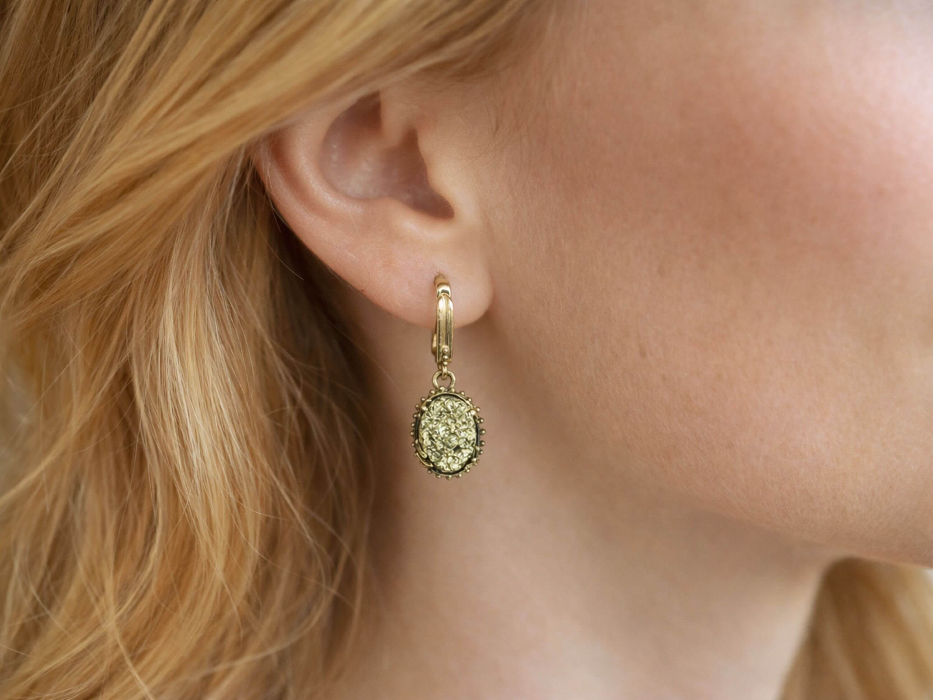 A model wearing Akra Gems golden pyrite earrings, showing the elegant oval drop and how the metallic shimmer complements the face