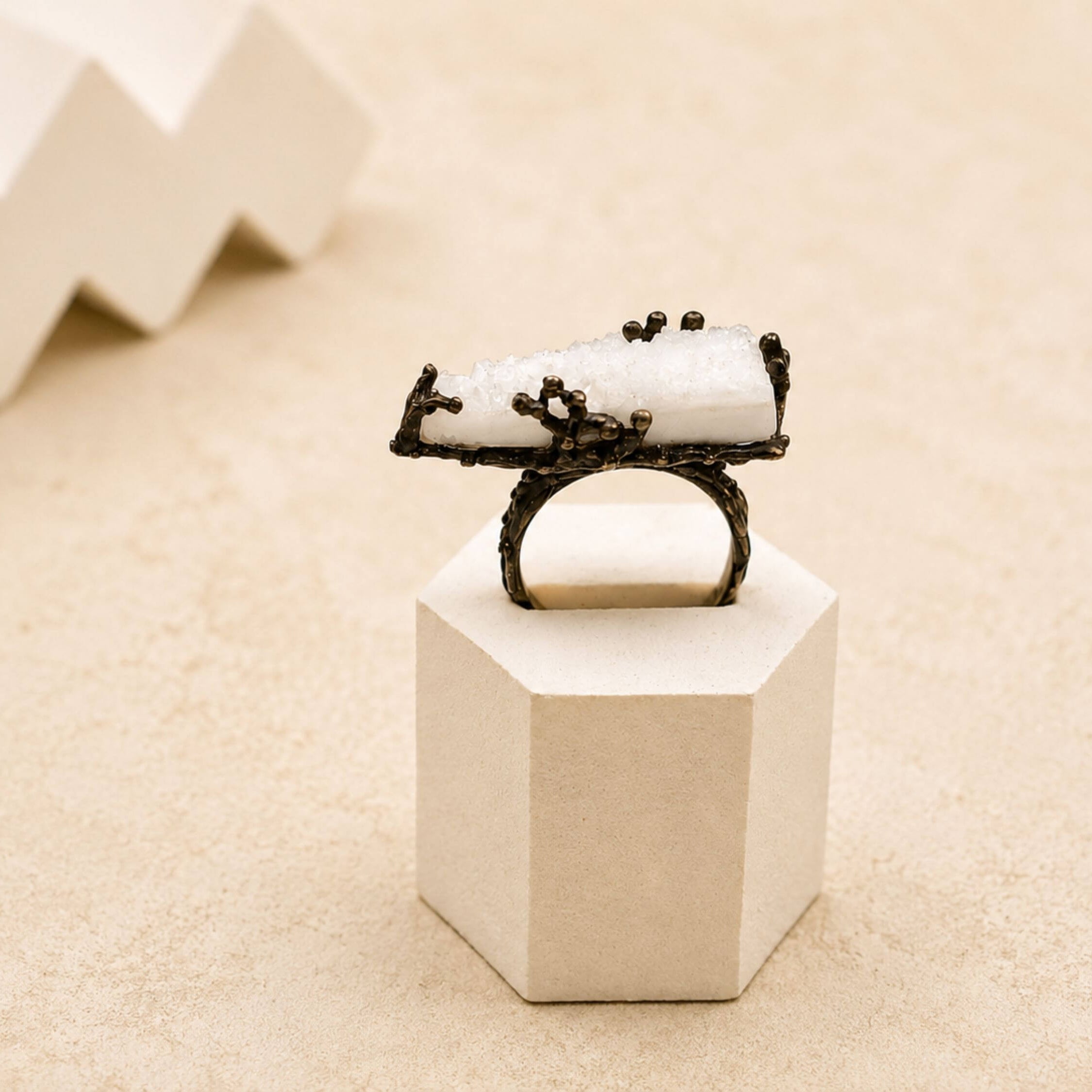 A bold raw white Moonstone statement ring set in a dark oxidized sterling silver frame, displayed on a minimalist geometric stand.