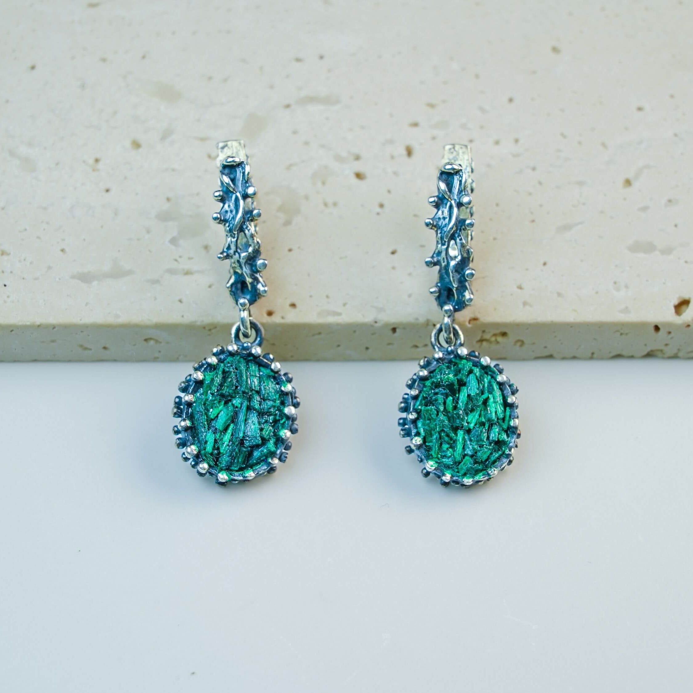 Vintage-style oval Malachite earrings in detailed sterling silver setting, showcasing natural green gemstone patterns on a soft beige background