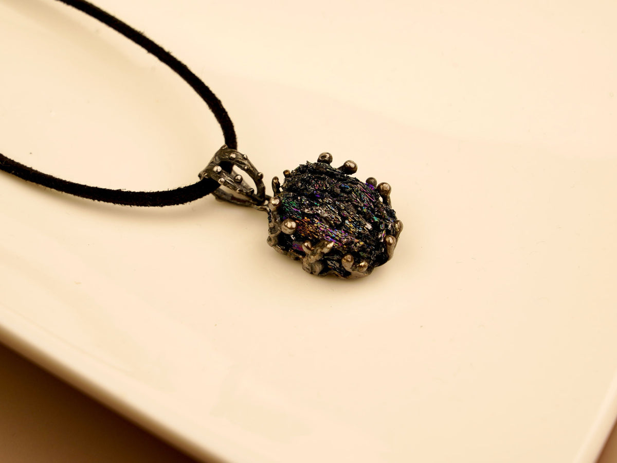 Raw black obsidian pendant in handcrafted sterling silver on a black cord, showing the natural iridescent surface of the stone