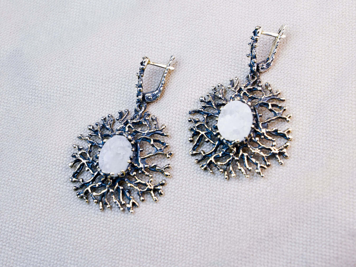 Two white moonstone ovals on textured cloth, each set in a round silver frame of fine branching arms