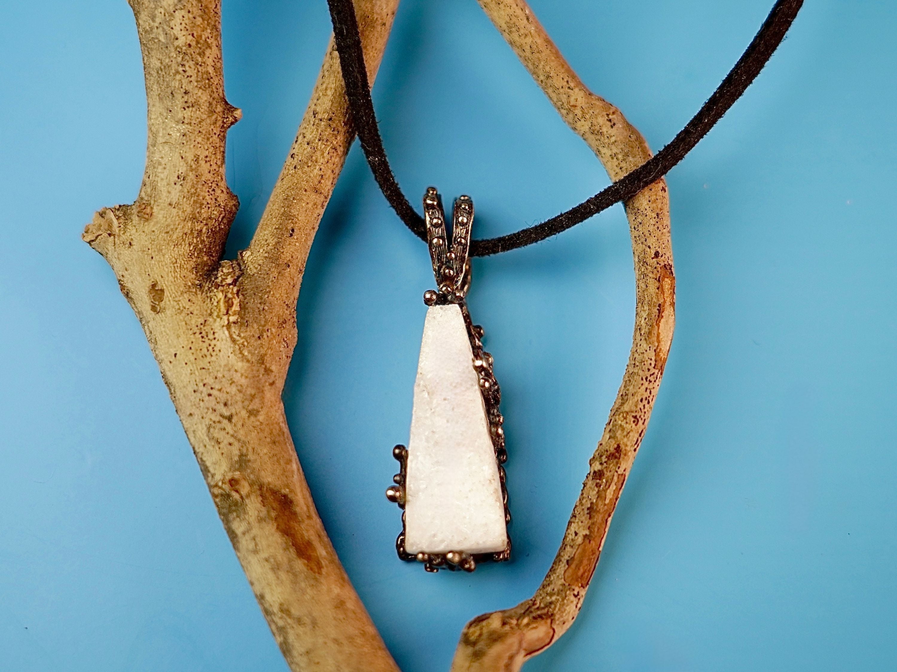 Raw white moonstone pendant necklace hanging on a natural wooden branch close up