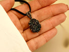 Close-up of a handcrafted raw black crystal pendant held in hand, showing the scale and unique texture of the Obsidian stone