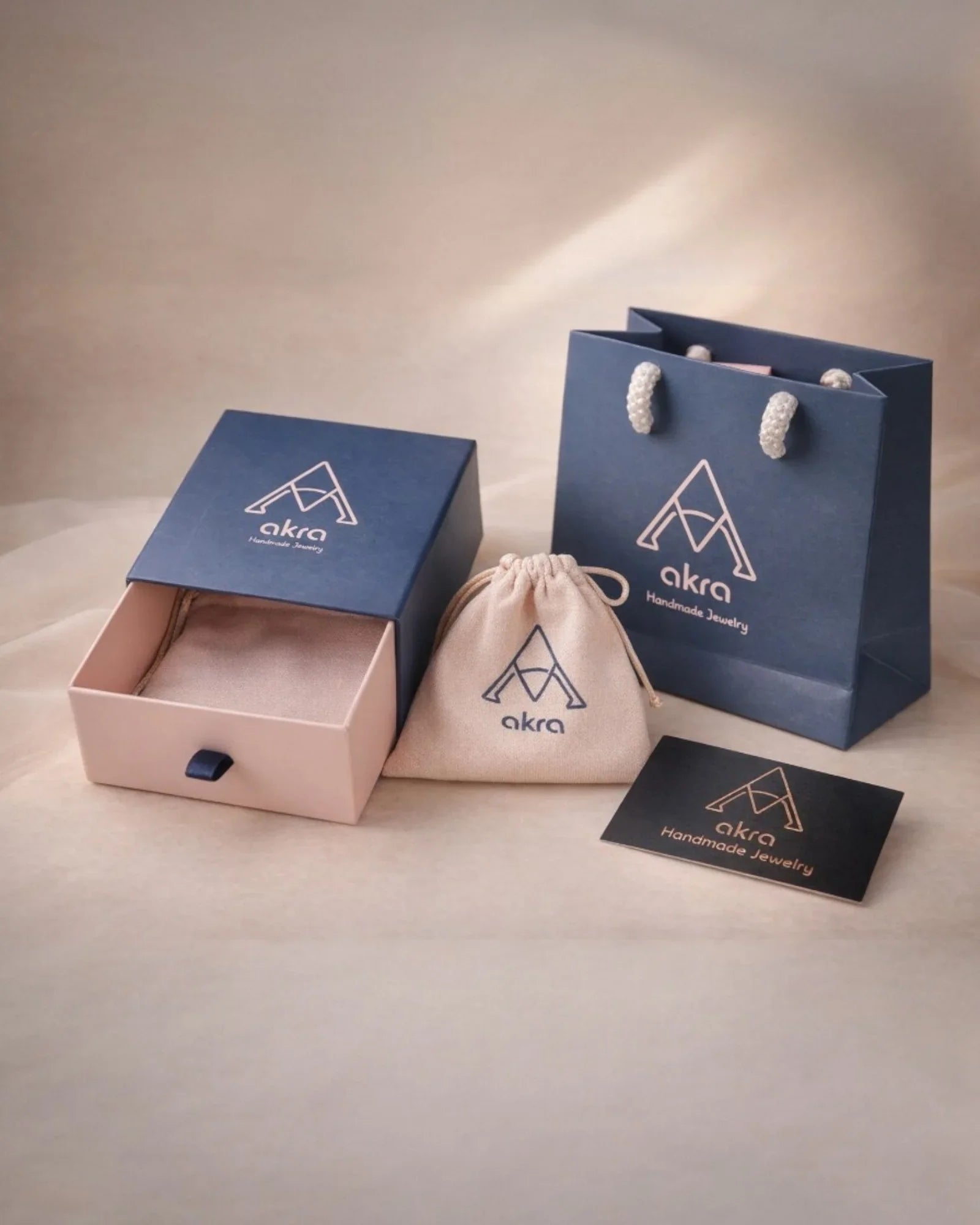 Premium AKRA jewelry gift packaging set featuring a branded navy blue shopping bag, a sliding drawer box, a soft fabric pouch, and a business card.