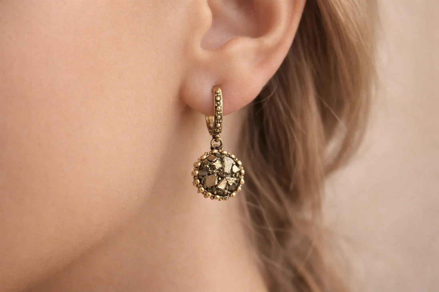 Close-up of a model wearing AKRA's handcrafted gold-toned drop earrings featuring a unique textured gemstone design.