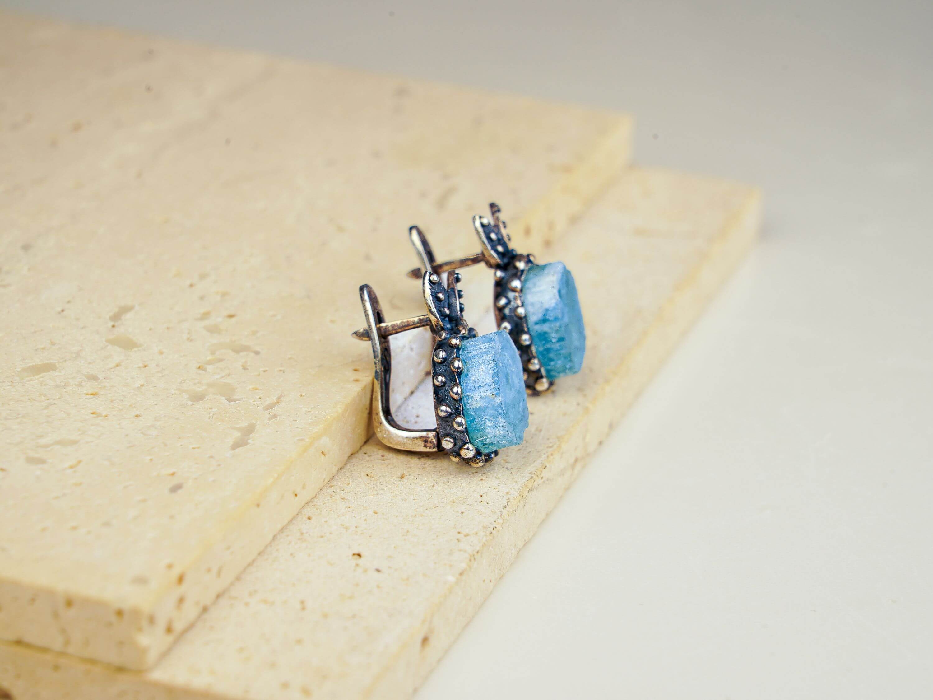 Frontal view of the bohemian style aquamarine earrings on a textured stone surface