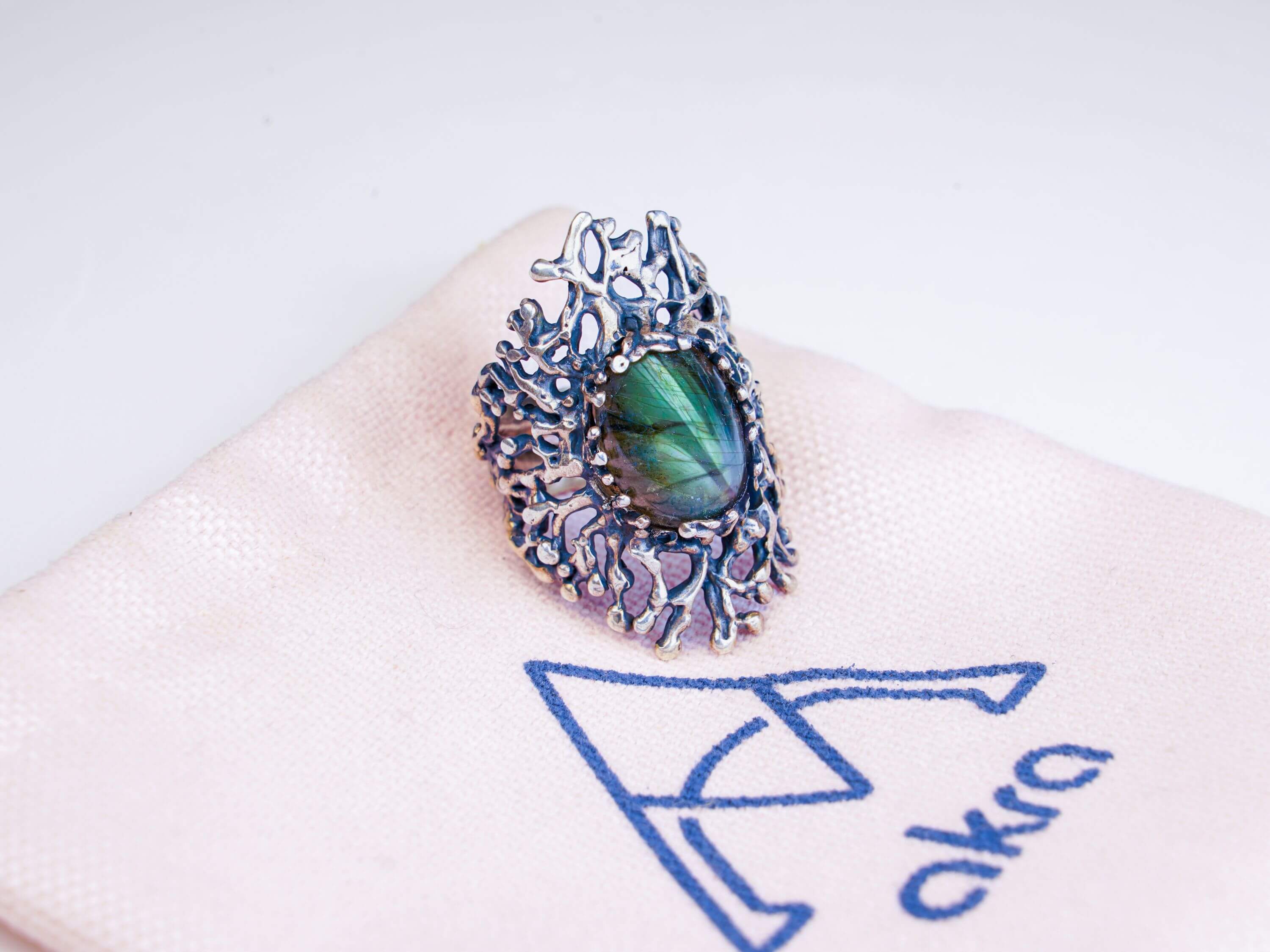Mystical labradorite gemstone ring displayed on a branded Akra pink jewelry pouch