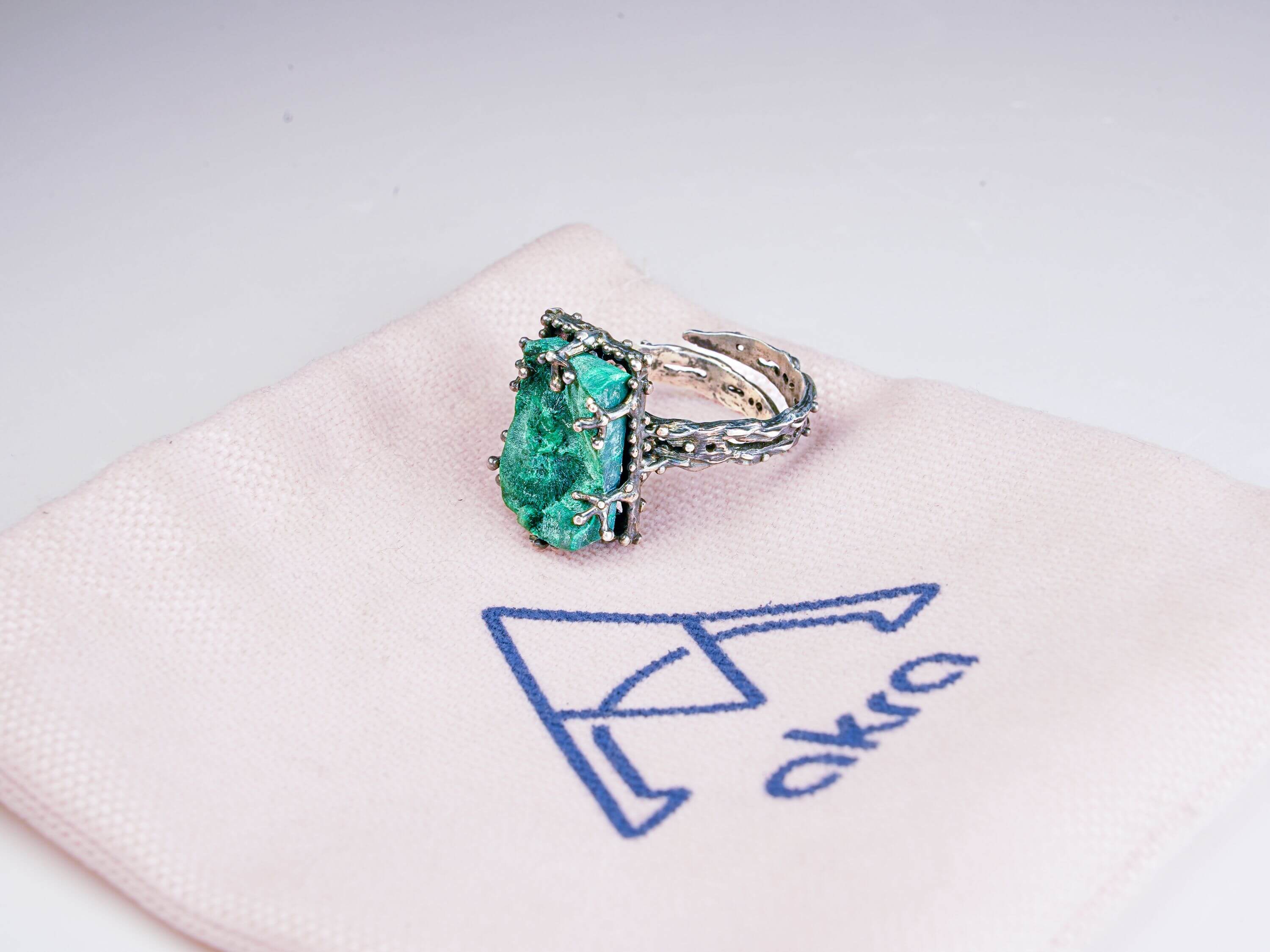 Handcrafted gemstone jewelry presentation with malachite ring on branded Akra jewelry pouch