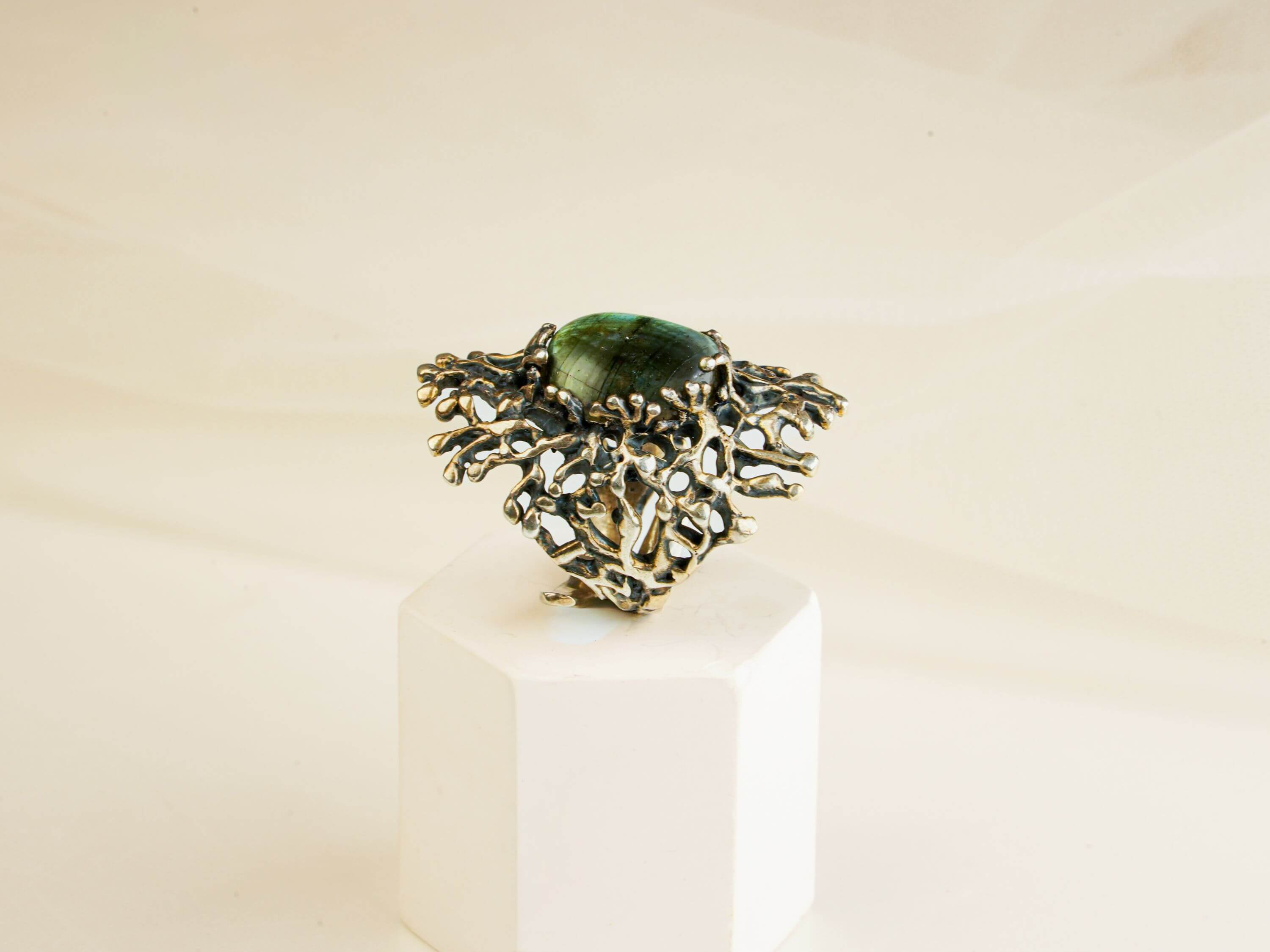 Artistic presentation of a rectangular iridescent labradorite ring on a white aesthetic pedestal