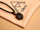 Obsidian black crystal pendant resting on a branded AKRA jewelry pouch, ideal for safe storage or gifting