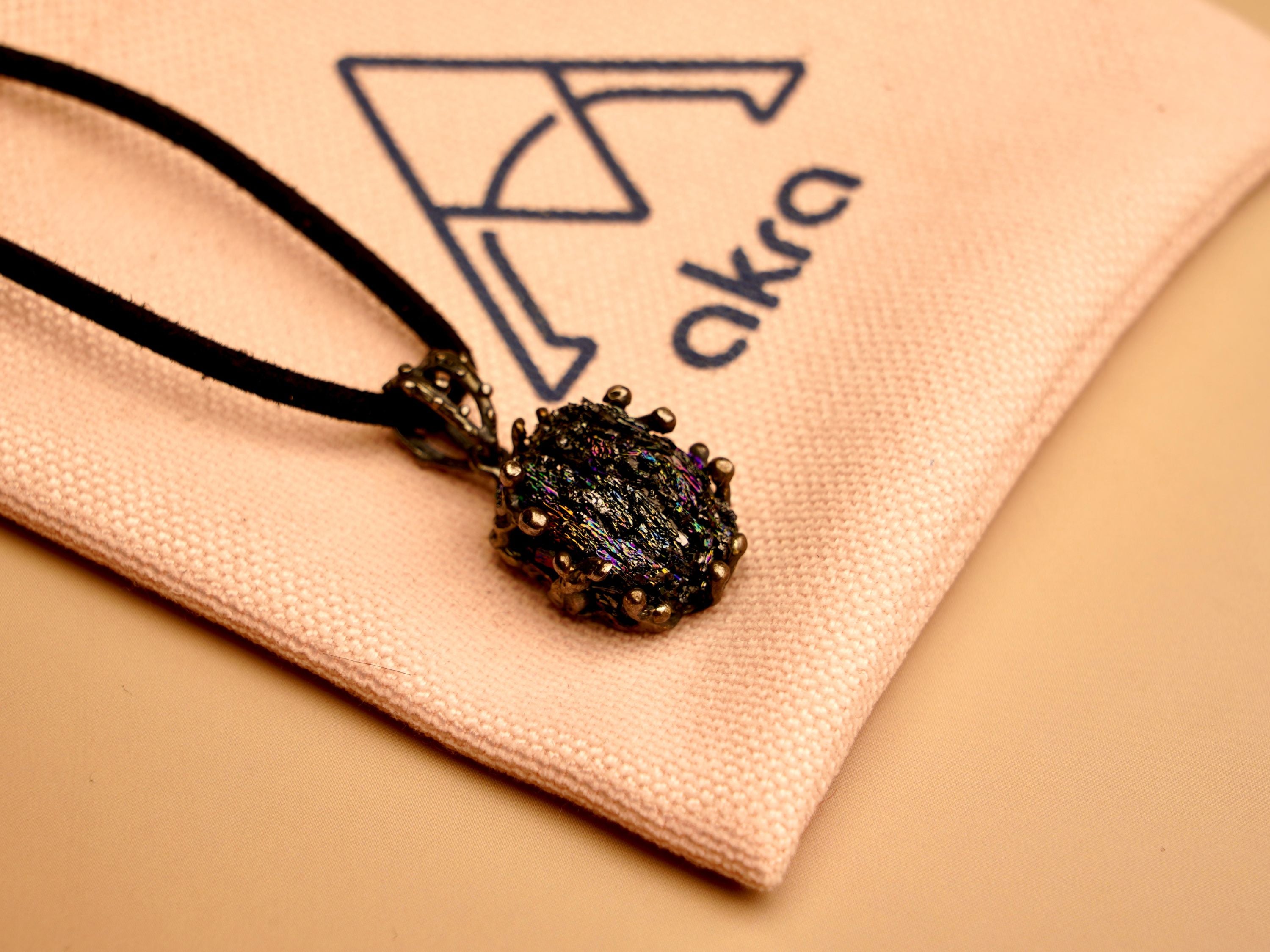 Obsidian black crystal pendant resting on a branded AKRA jewelry pouch, ideal for safe storage or gifting