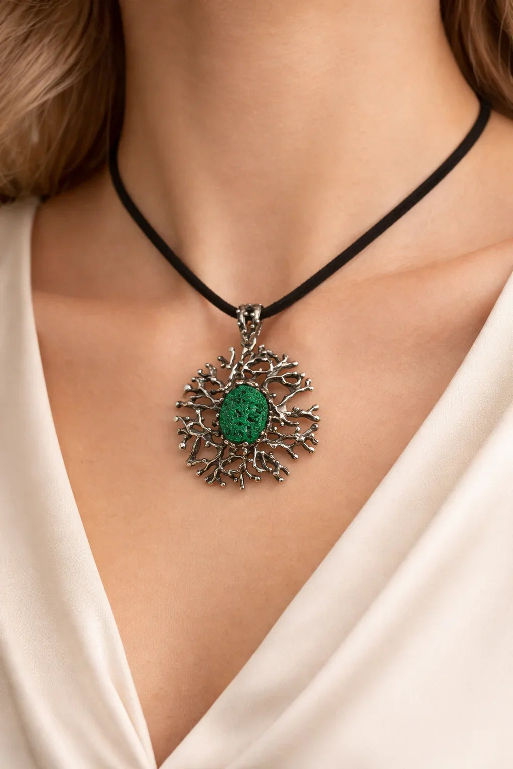 Lifestyle shot of a model wearing AKRA's large malachite necklace with an intricate sterling silver coral-inspired pendant on a black cord.