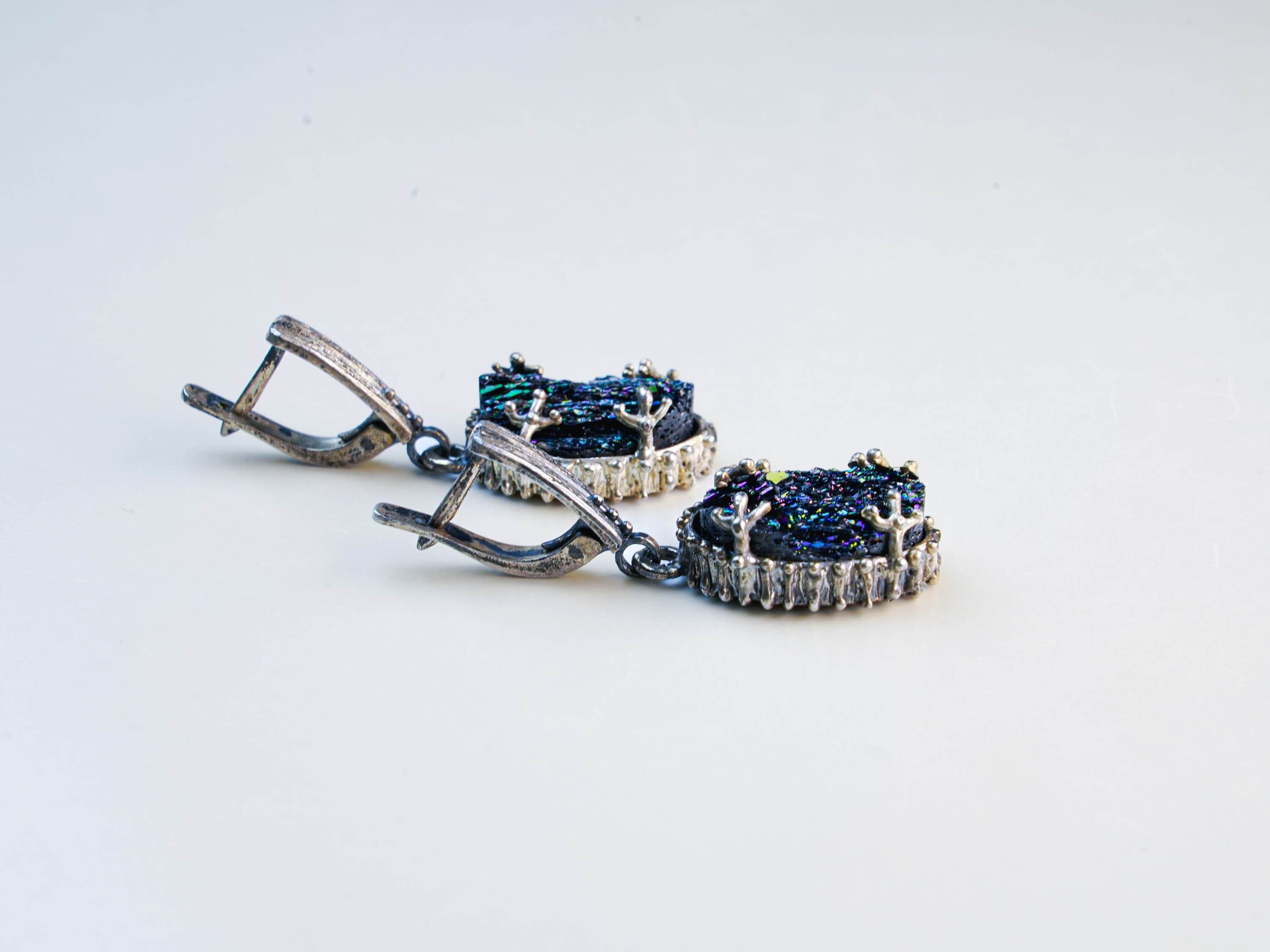 Side-angle view of the earrings under soft light, highlighting the depth of the raw crystal and the ornate silver detailing