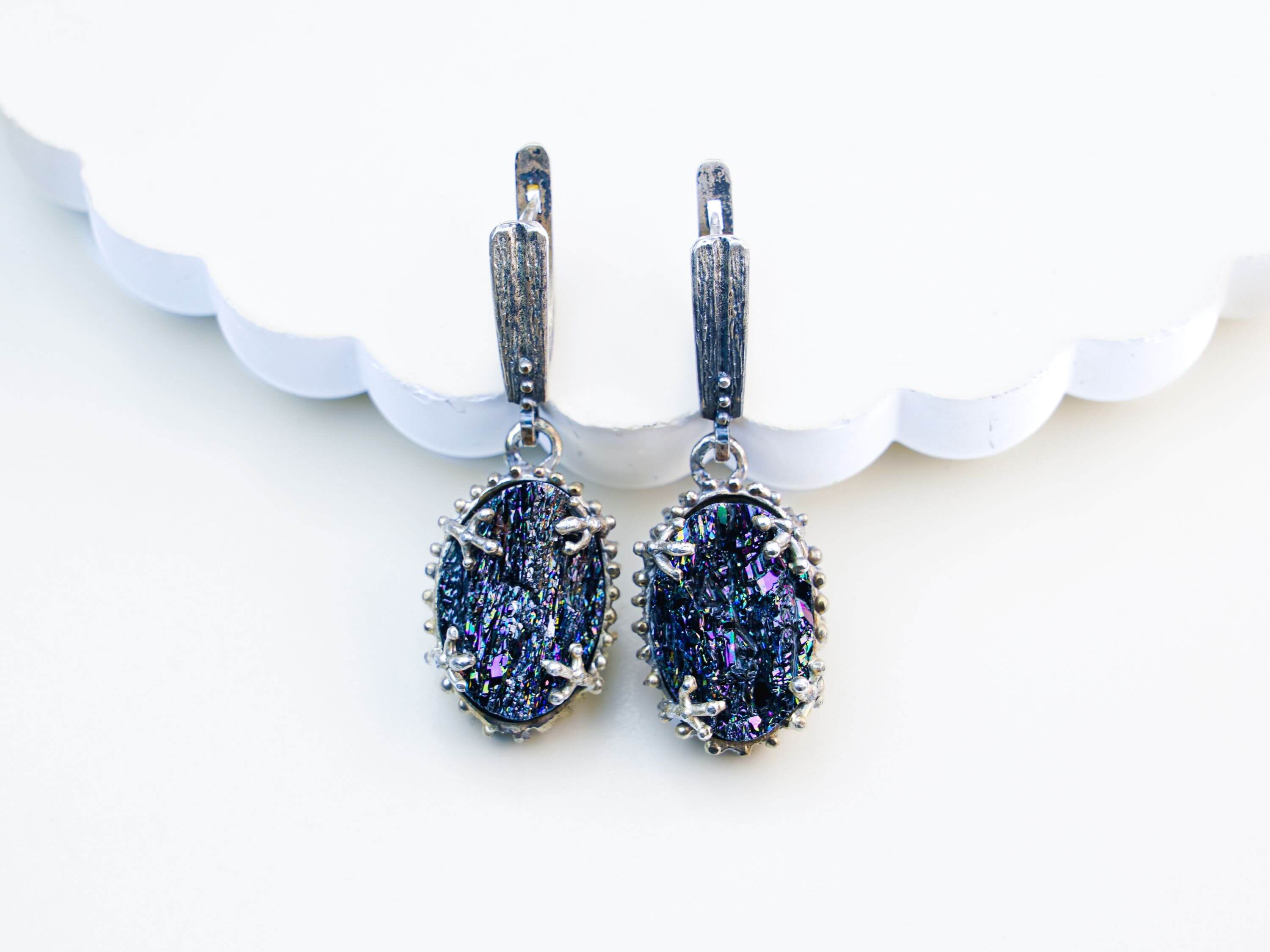 Oval Black Tourmaline earrings featuring raw crystalline gemstones in an ornate sterling silver frame, shot on a clean beige background