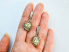 Two golden pyrite statement earrings held in a hand to illustrate their perfect oval scale and handcrafted silver detailing