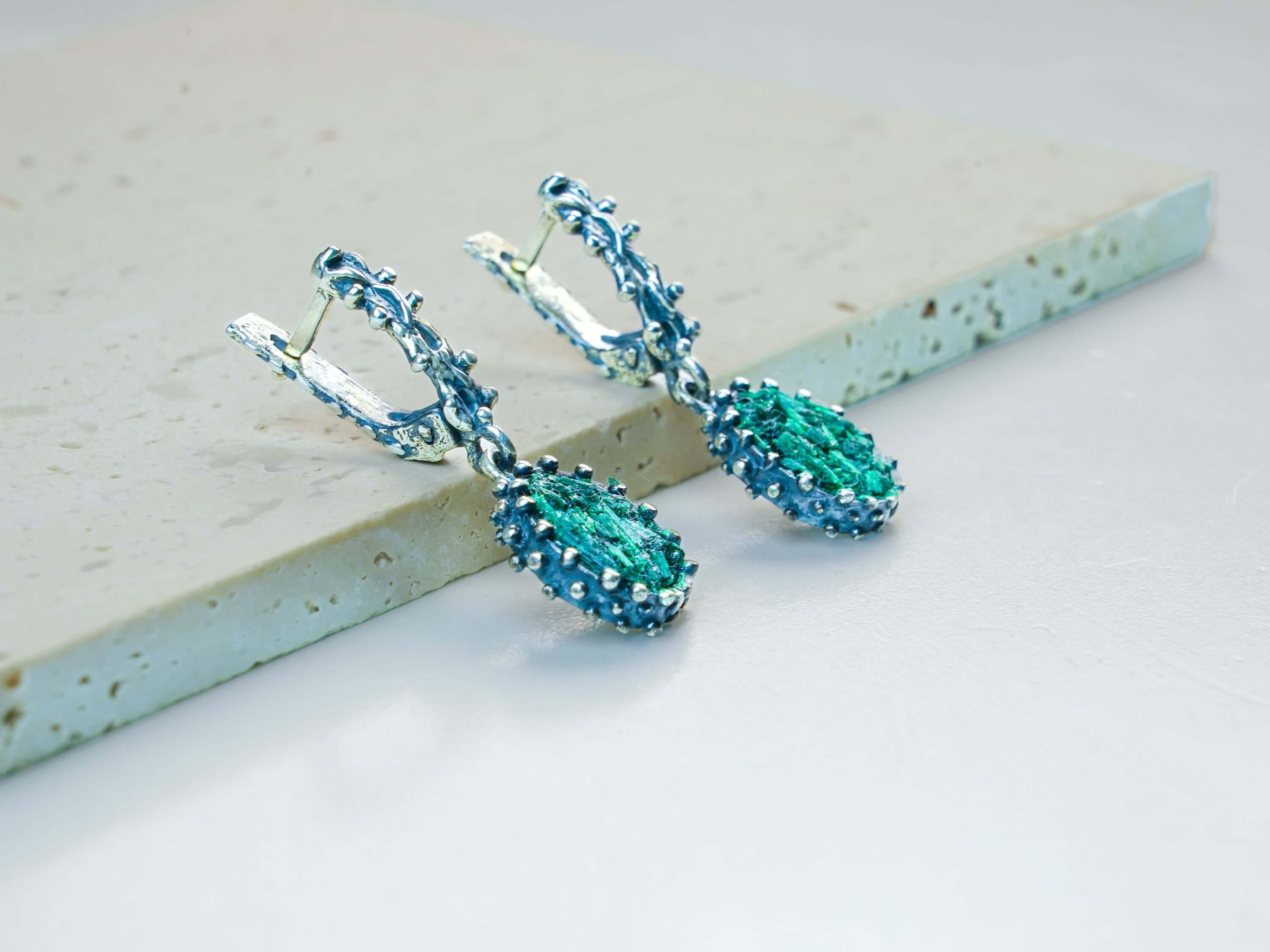 Handmade Akra Gems Malachite earrings resting alongside other pieces from the green gemstone collection, crafted in Tbilisi, Georgia