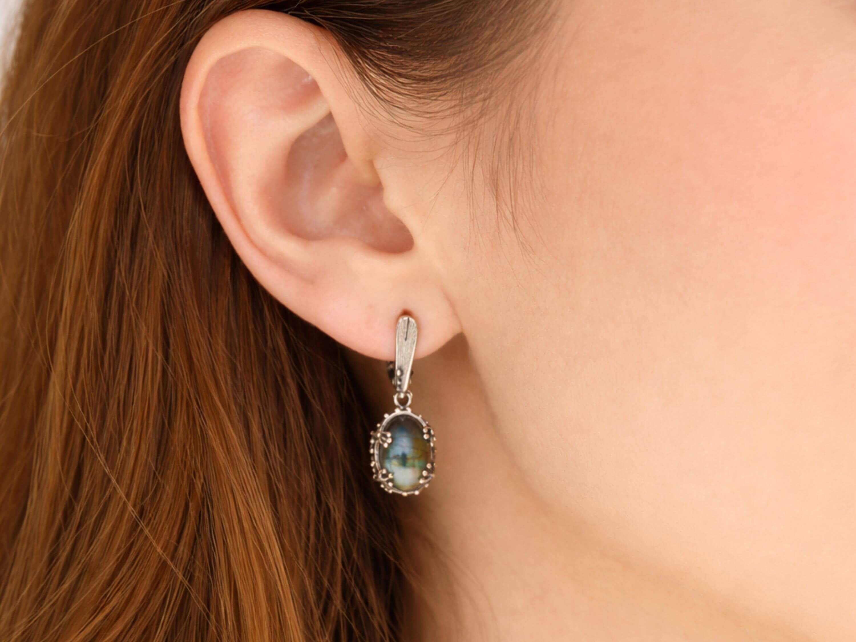 Handmade labradorite earrings worn on ear, showcasing the elegant drop style and blue gemstone flash
