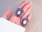A pair of large Moonstone branch earrings held in a hand to demonstrate their impressive statement size and artisan quality