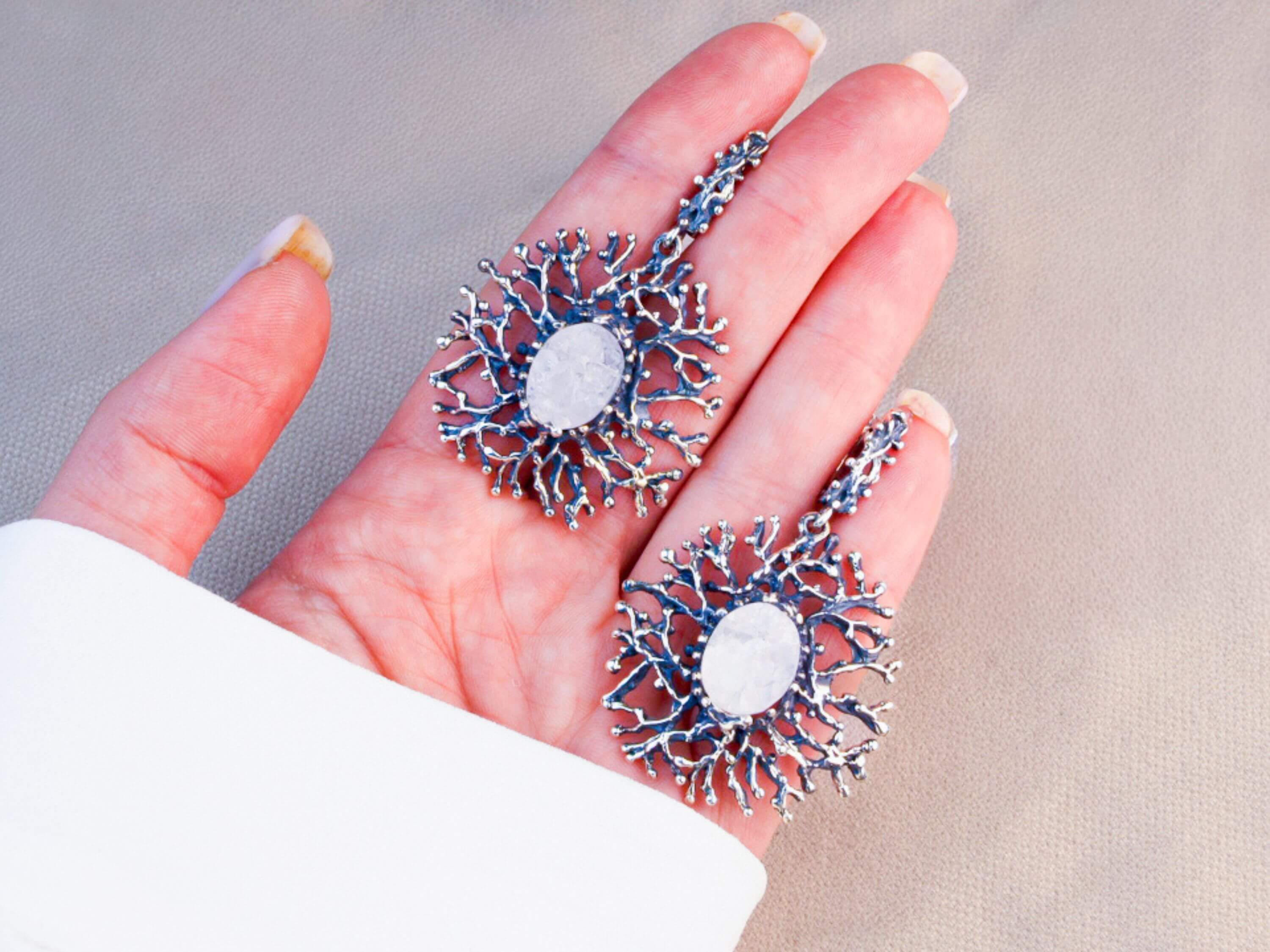 A pair of large Moonstone branch earrings held in a hand to demonstrate their impressive statement size and artisan quality