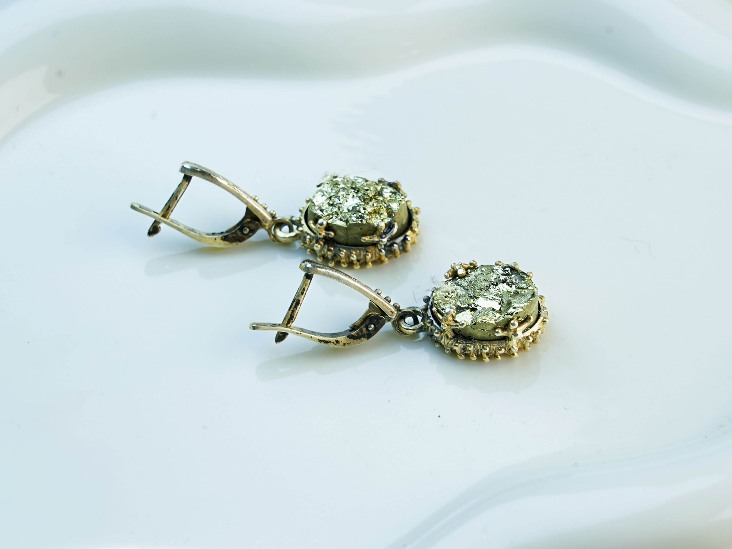Side profile of the oval pyrite earrings, showing the depth of the stone and the intricate texture of the silver setting