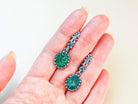 A pair of Akra Gems handcrafted oval Malachite earrings held in a hand to demonstrate the physical scale and artisan craftsmanship