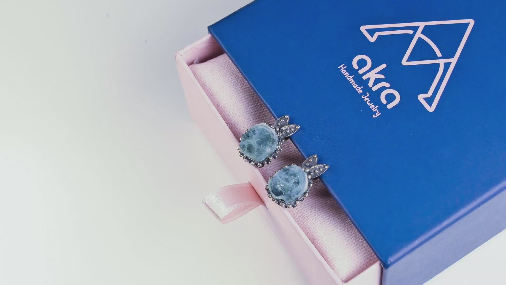 Cinematic showcase of the blue aquamarine earrings catching the light, highlighting the silver details and gemstone clarity