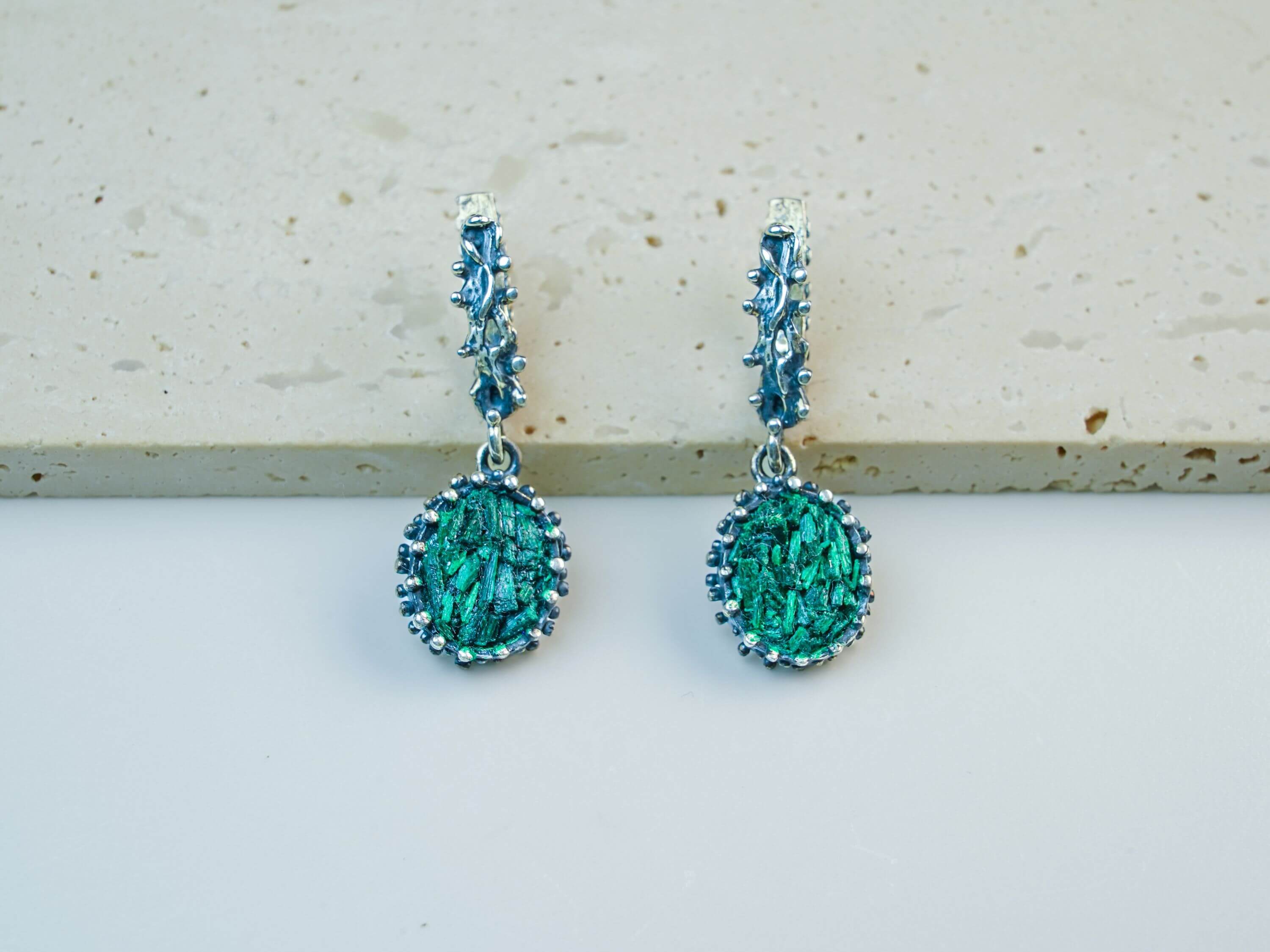 Vintage-style oval Malachite earrings in detailed sterling silver setting, showcasing natural green gemstone patterns on a soft beige background